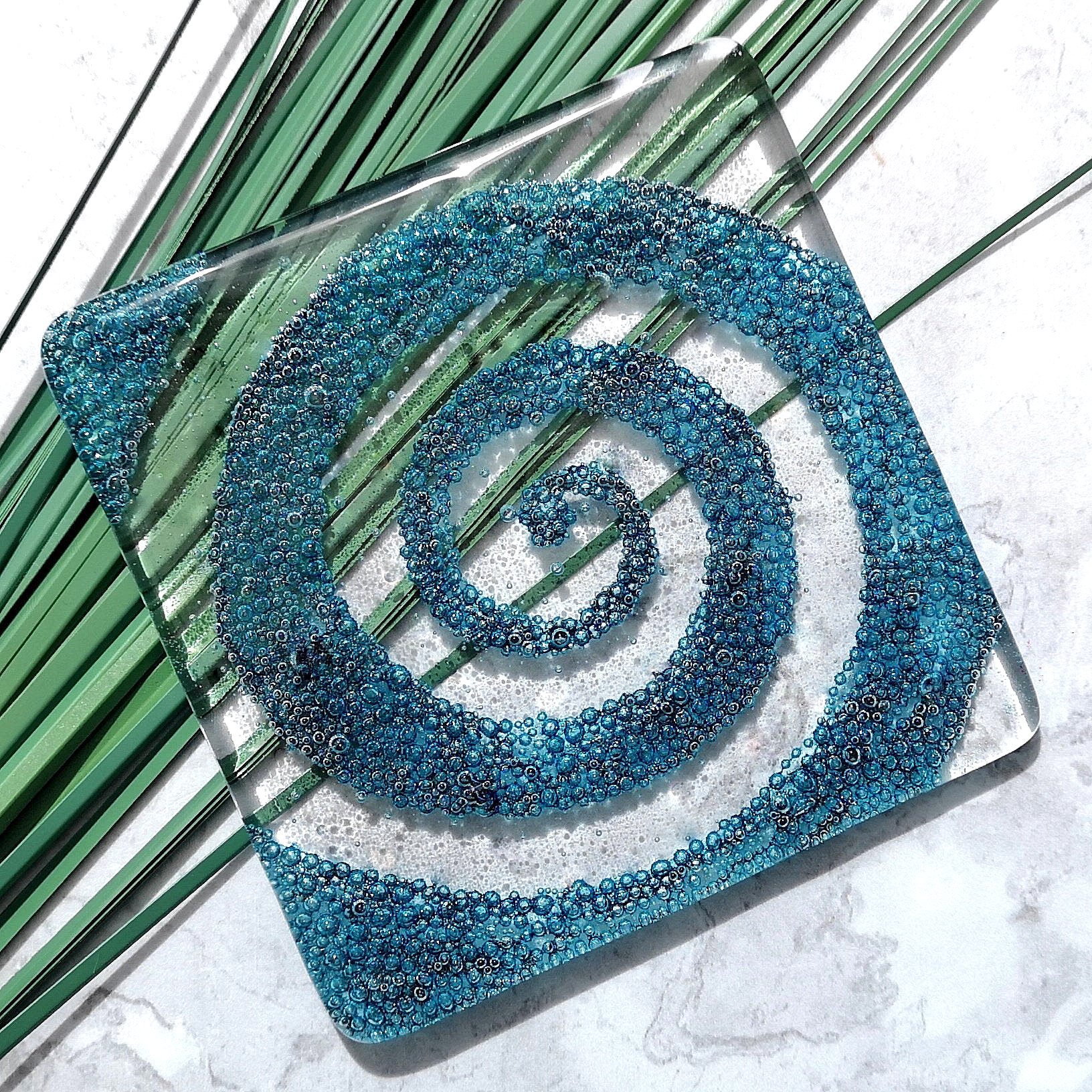Handmade fused glass spiral drinks coaster with embedded coloured bubbles. Glass wall tile, hot drink table mat, twirl design, swirly pattern gift. Bubbly home decoration, dining table protection.