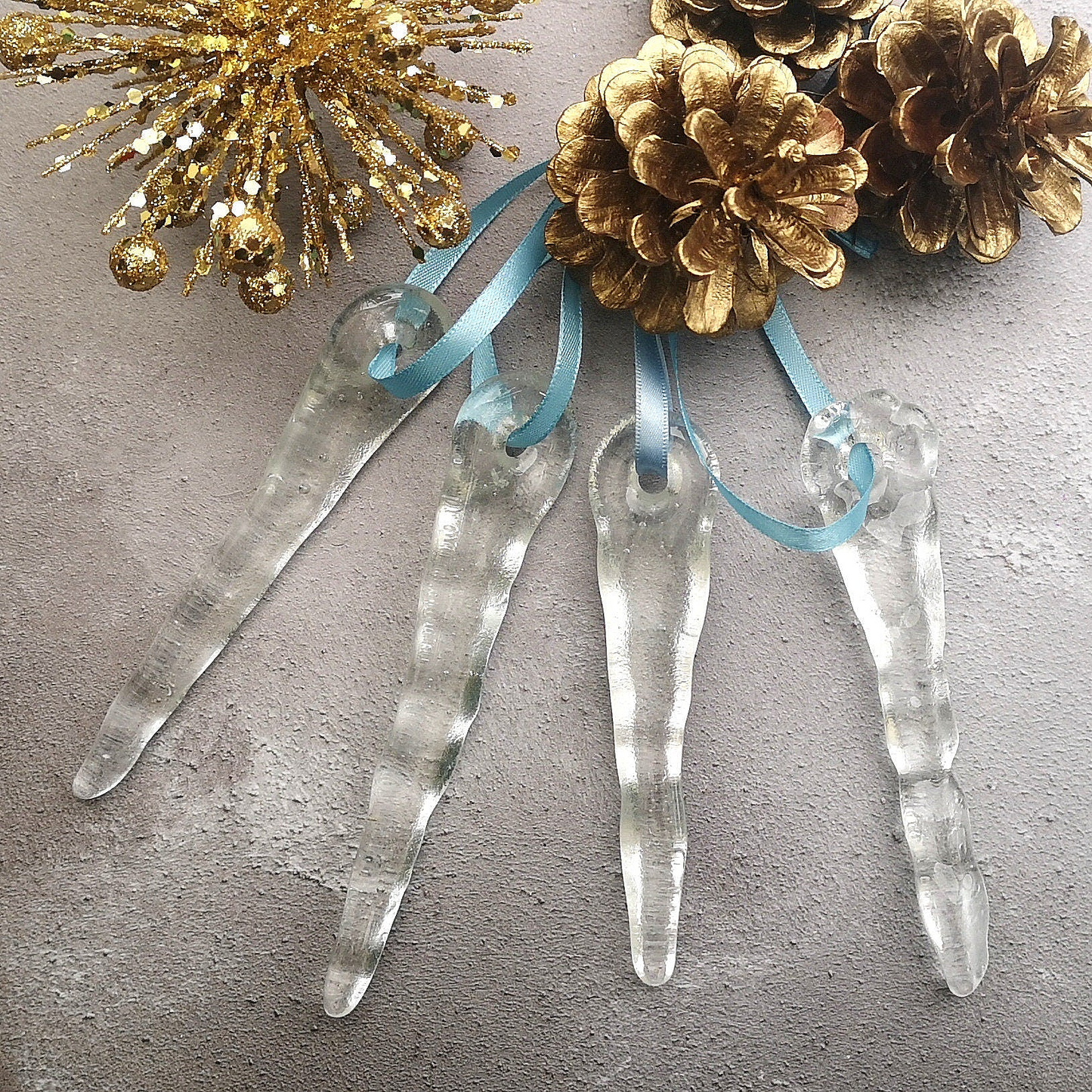 Clear glass icicles displayed against a background with festive decorations, showing their wintry charm. Perfect for a unique holiday gift.