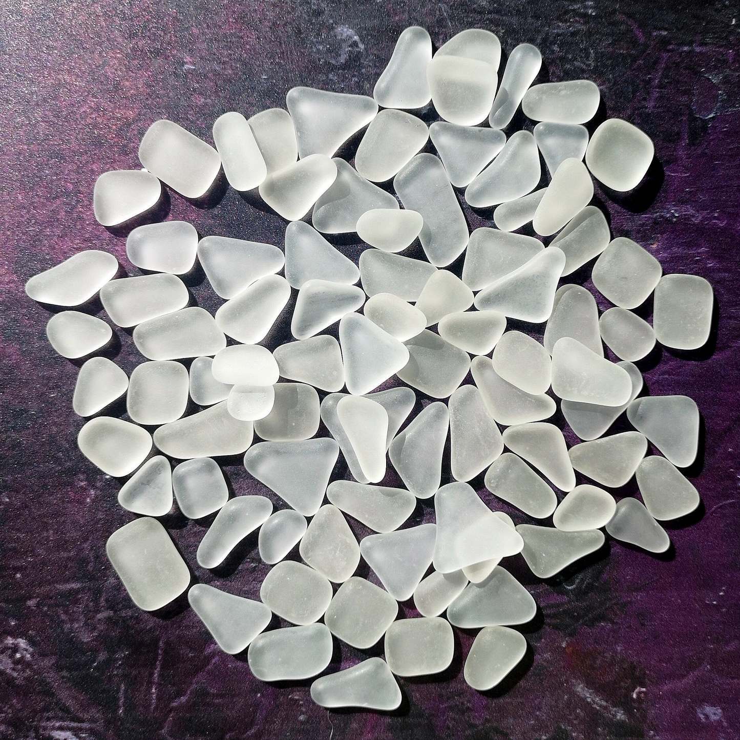 Pile of frosted white tumbled glass pieces, resembling weathered sea glass, contrasted against a dark background for a striking visual effect