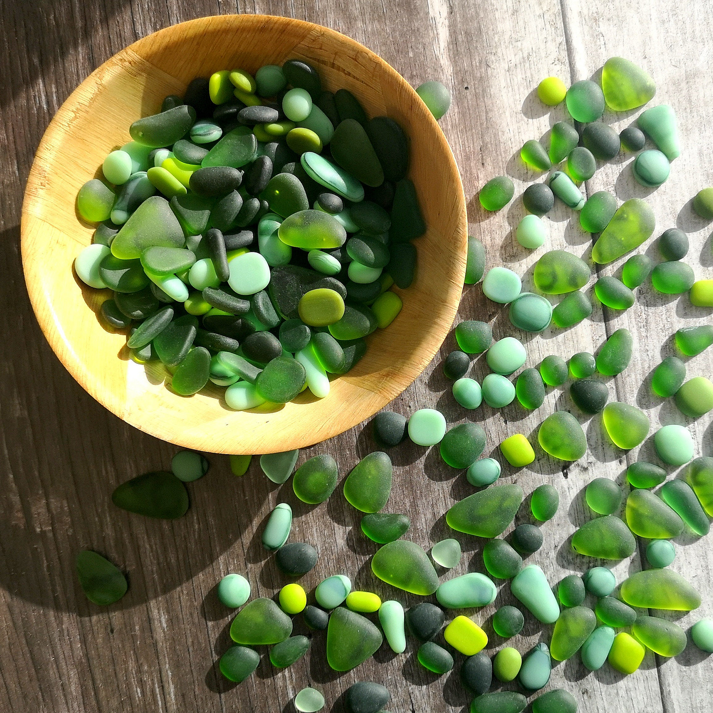 A bowl full of tumbled glass in green hues, highlighting the frosted finish and varied shapes, perfect for creative DIY projects