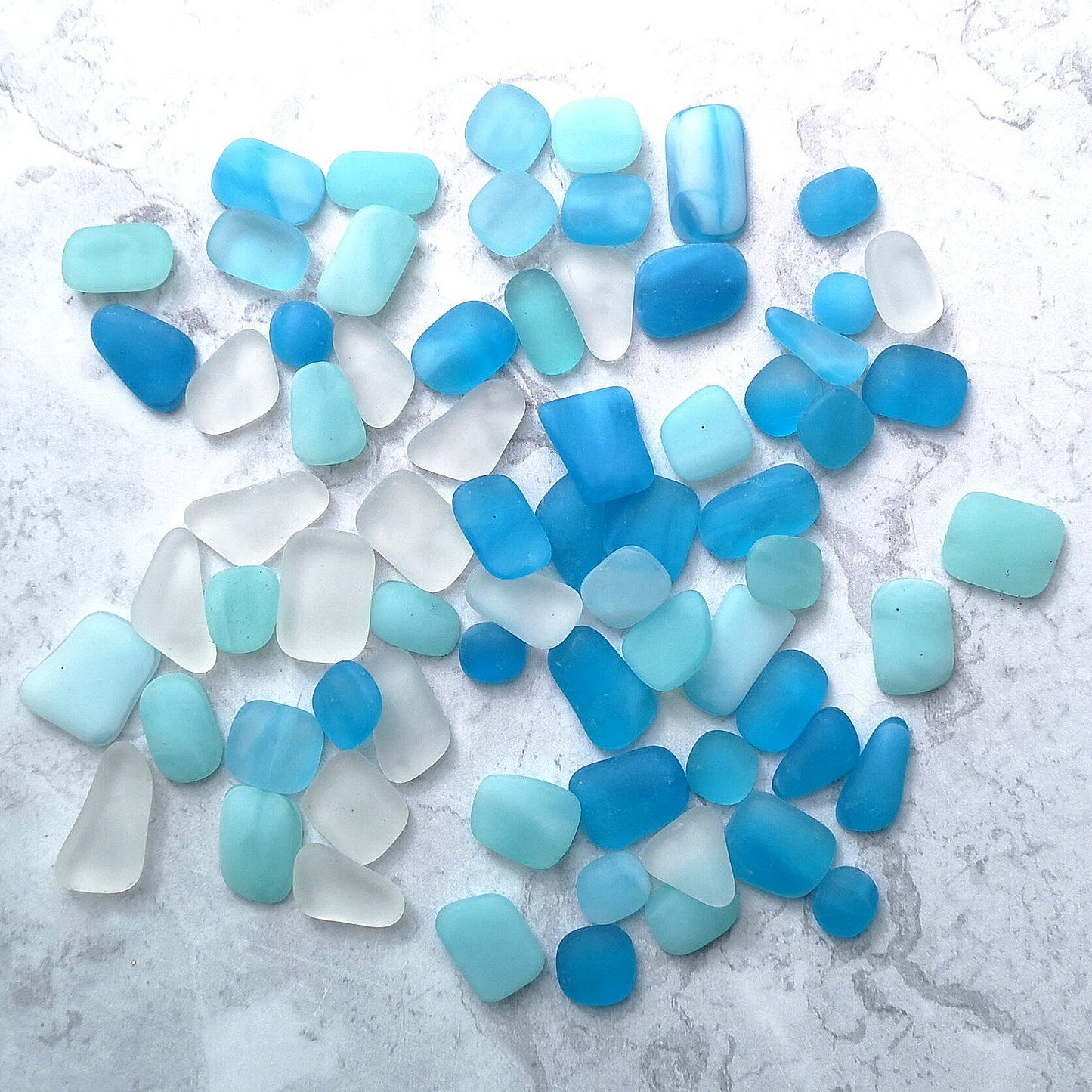Collection of weathered sea glass-like tumbled pieces in serene blue and turquoise tones, contrasted against a simple background for visual impact