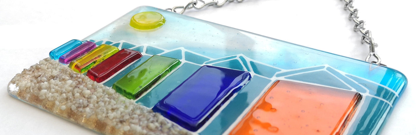 Handmade fused glass 3D Beach Huts Hanging Picture. Seaside suncatcher wall art, beach gift decoration, sea ocean scene with glass pebbles, rainbow coloured beach huts, sun and blue sky.