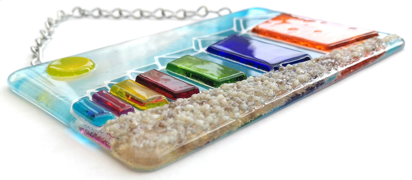 Handmade fused glass 3D Beach Huts Hanging Picture. Seaside suncatcher wall art, beach gift decoration, sea ocean scene with glass pebbles, rainbow coloured beach huts, sun and blue sky.