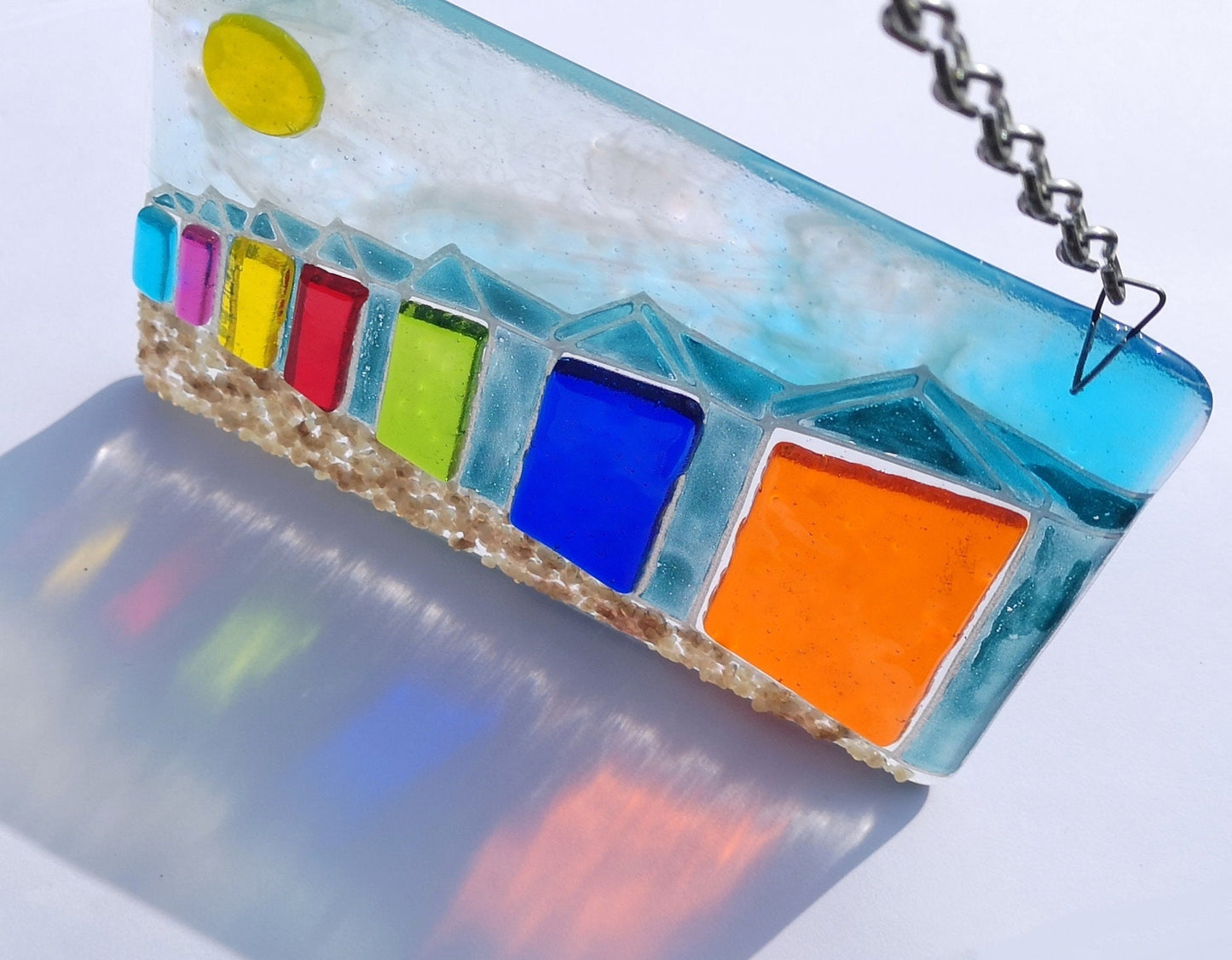Handmade fused glass 3D Beach Huts Hanging Picture. Seaside suncatcher wall art, beach gift decoration, sea ocean scene with glass pebbles, rainbow coloured beach huts, sun and blue sky.