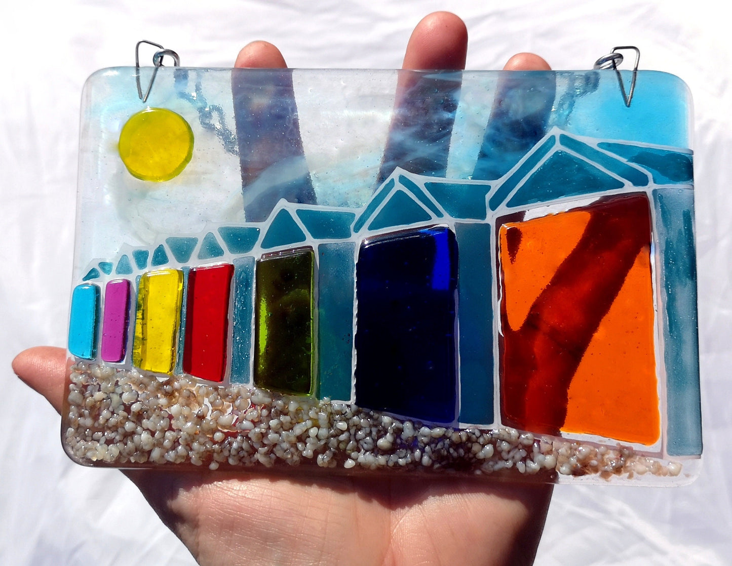 Handmade fused glass 3D Beach Huts Hanging Picture. Seaside suncatcher wall art, beach gift decoration, sea ocean scene with glass pebbles, rainbow coloured beach huts, sun and blue sky.