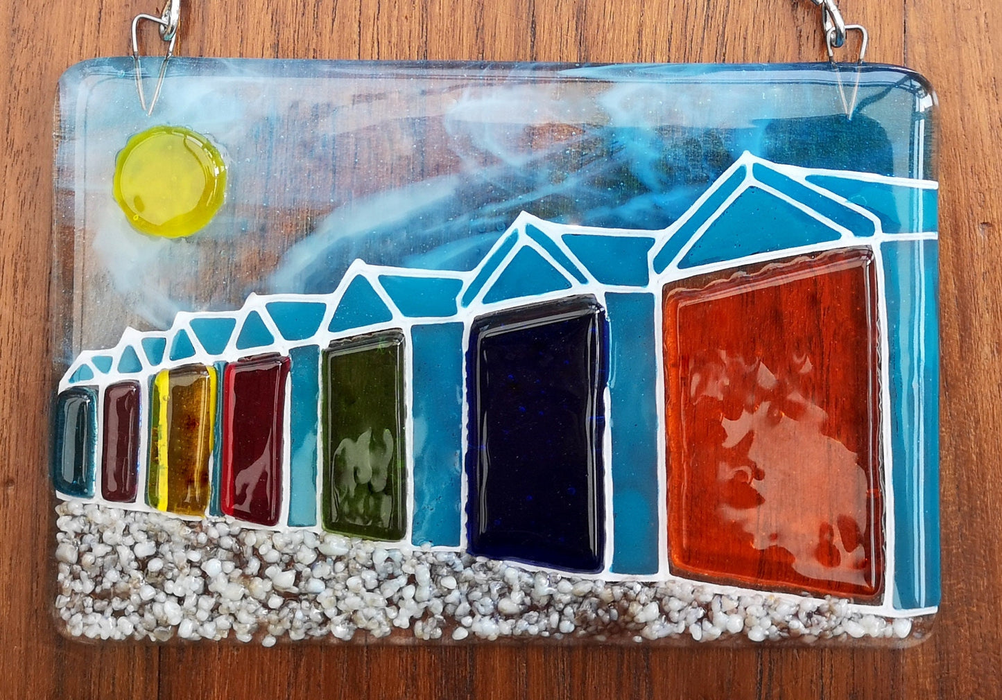 Handmade fused glass 3D Beach Huts Hanging Picture. Seaside suncatcher wall art, beach gift decoration, sea ocean scene with glass pebbles, rainbow coloured beach huts, sun and blue sky.