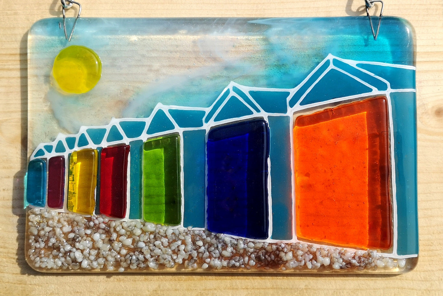 Handmade fused glass 3D Beach Huts Hanging Picture. Seaside suncatcher wall art, beach gift decoration, sea ocean scene with glass pebbles, rainbow coloured beach huts, sun and blue sky.