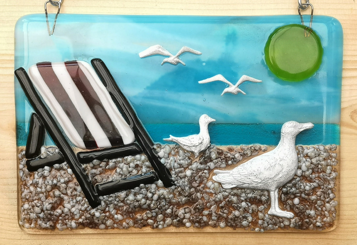 Handmade fused glass 3D Seagull & Deckchair Hanging Picture. Seaside suncatcher wall art, beach gift decoration, sea ocean scene with glass pebbles, sea birds, sun and blue sky.