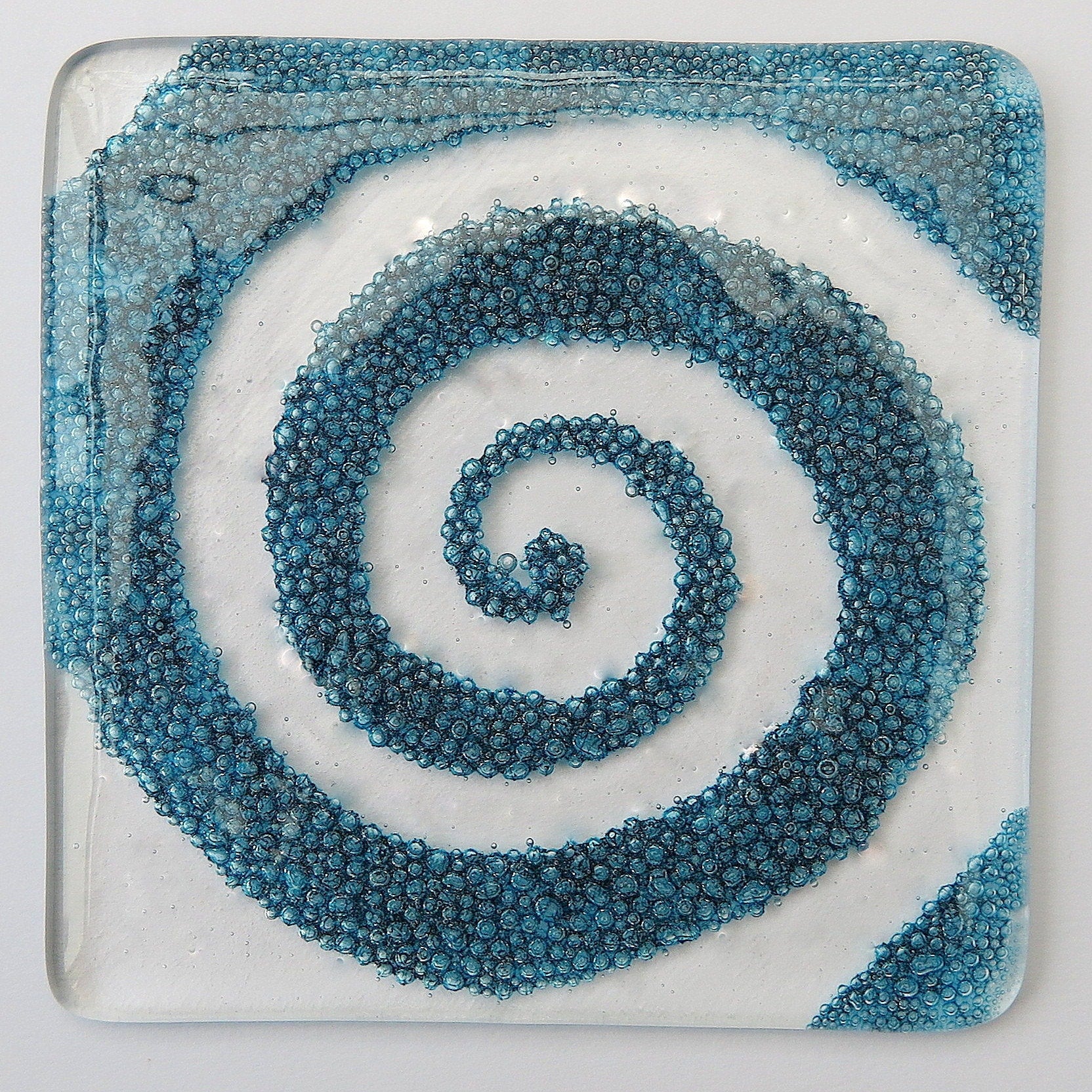 Handmade fused glass spiral drinks coaster with embedded coloured bubbles. Glass wall tile, hot drink table mat, twirl design, swirly pattern gift. Bubbly home decoration, dining table protection.