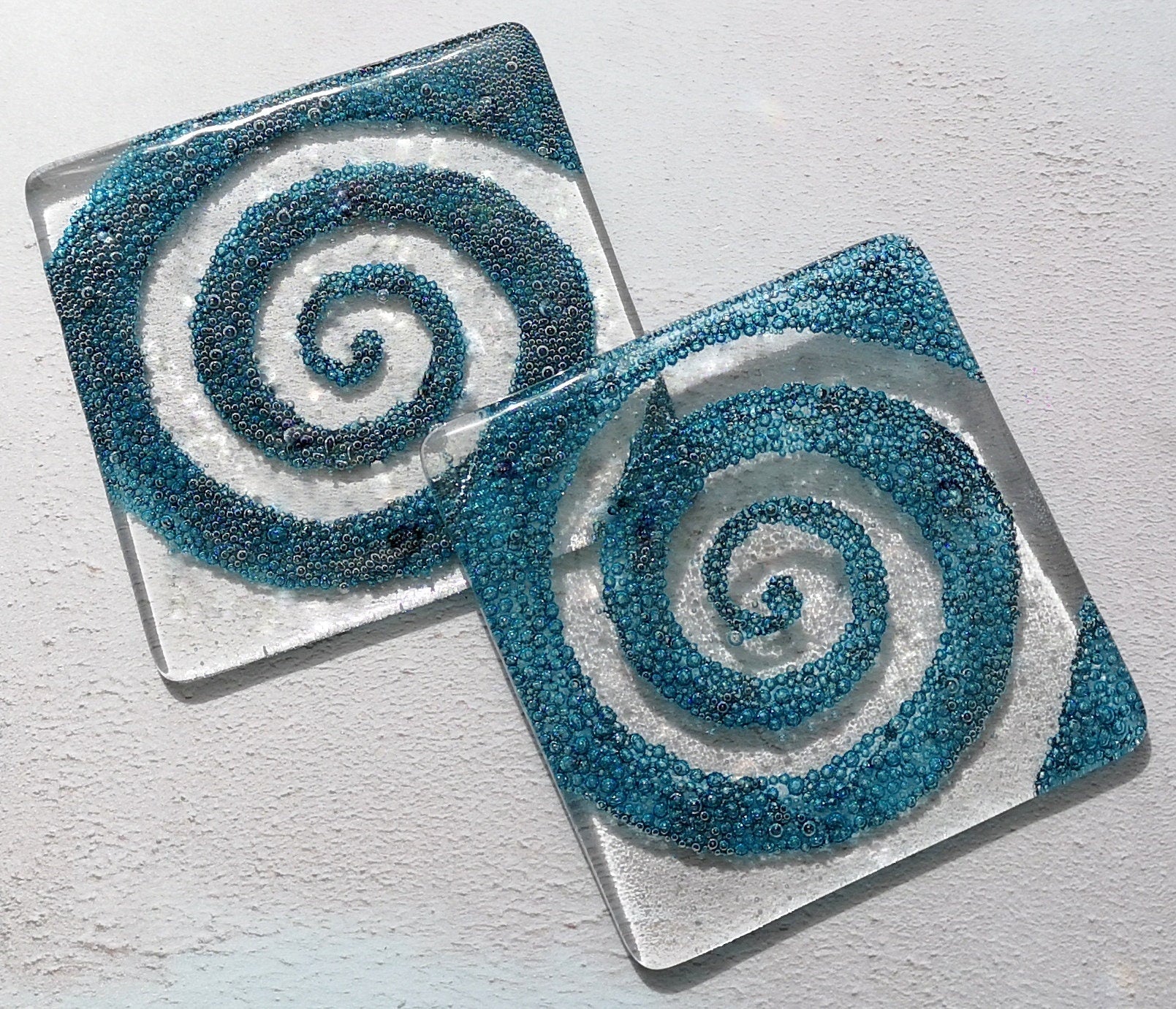 Handmade fused glass spiral drinks coaster with embedded coloured bubbles. Glass wall tile, hot drink table mat, twirl design, swirly pattern gift. Bubbly home decoration, dining table protection.