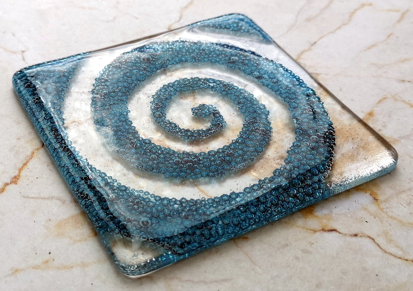 Handmade fused glass spiral drinks coaster with embedded coloured bubbles. Glass wall tile, hot drink table mat, twirl design, swirly pattern gift. Bubbly home decoration, dining table protection.
