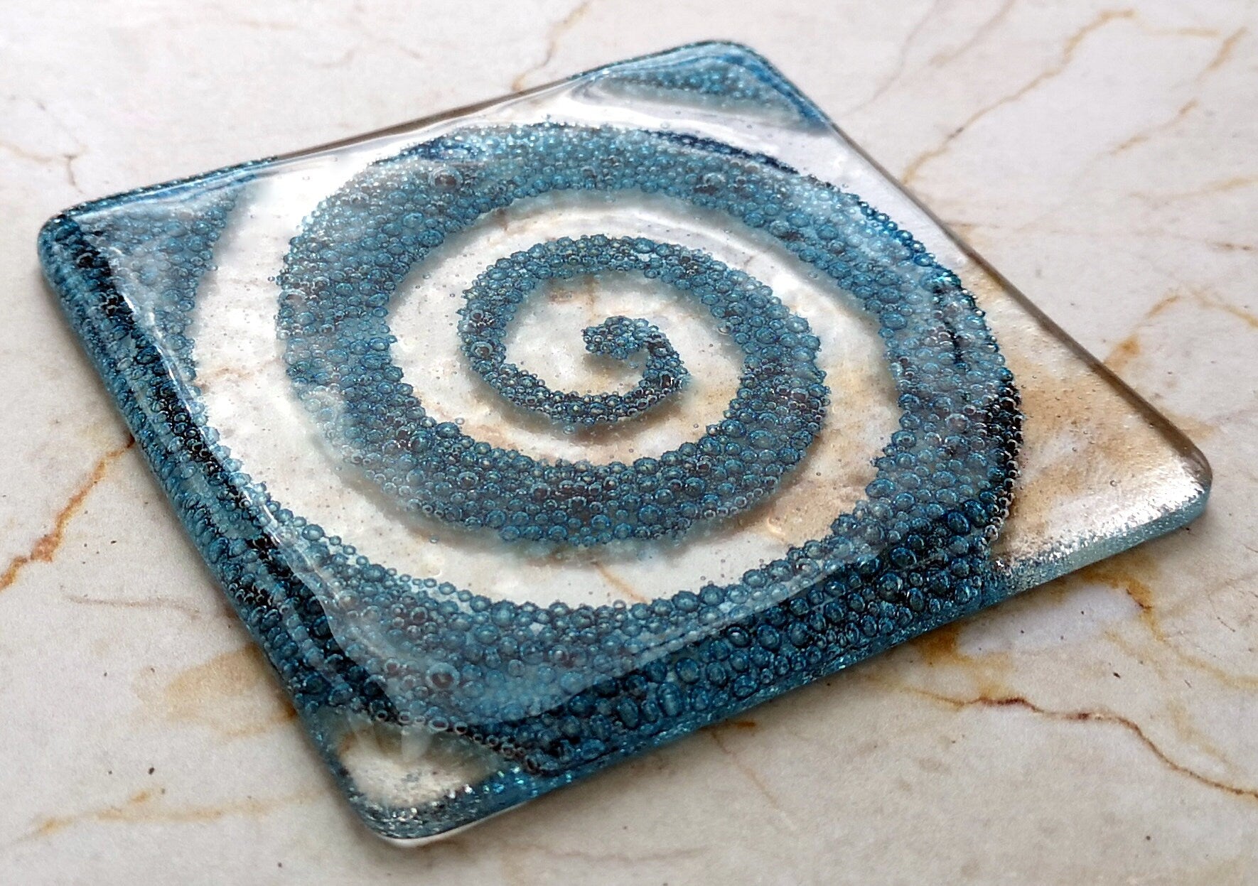 Handmade fused glass spiral drinks coaster with embedded coloured bubbles. Glass wall tile, hot drink table mat, twirl design, swirly pattern gift. Bubbly home decoration, dining table protection.
