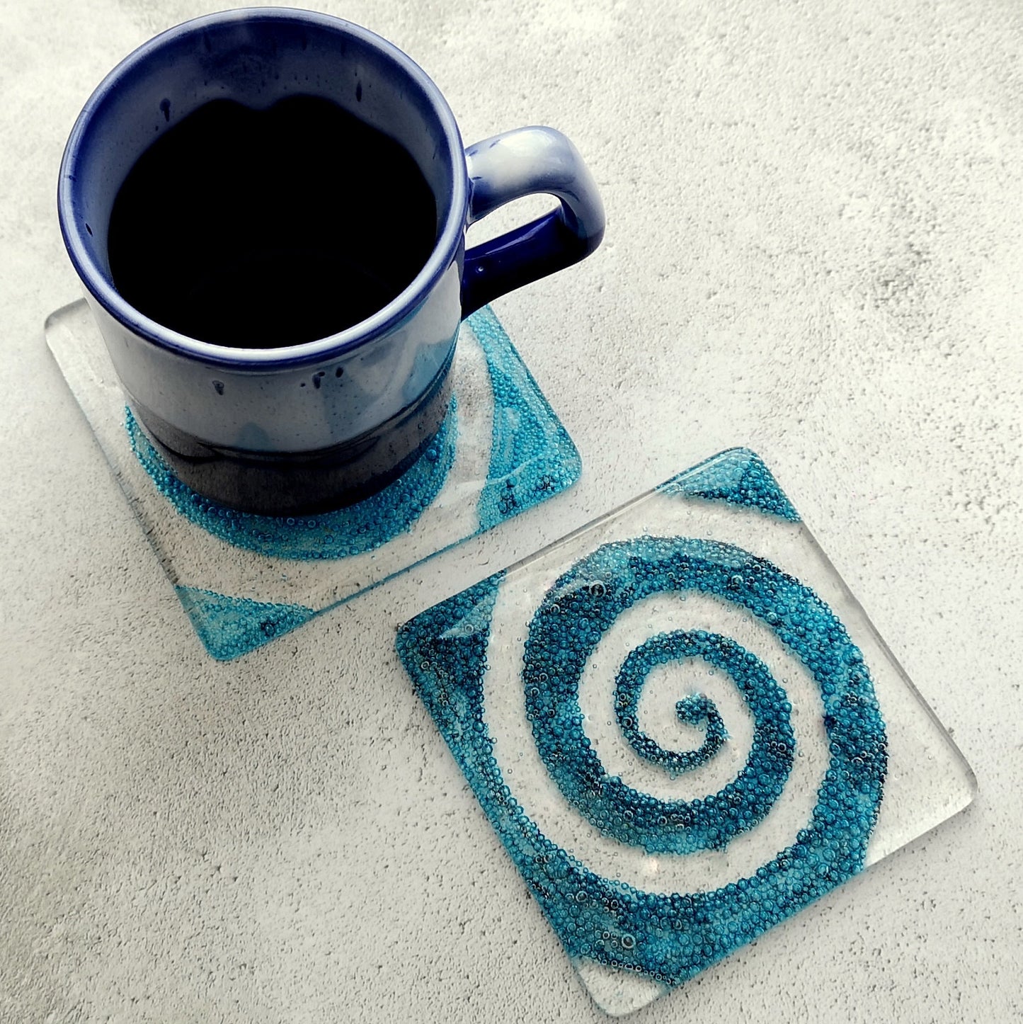 Handmade fused glass spiral drinks coaster with embedded coloured bubbles. Glass wall tile, hot drink table mat, twirl design, swirly pattern gift. Bubbly home decoration, dining table protection.