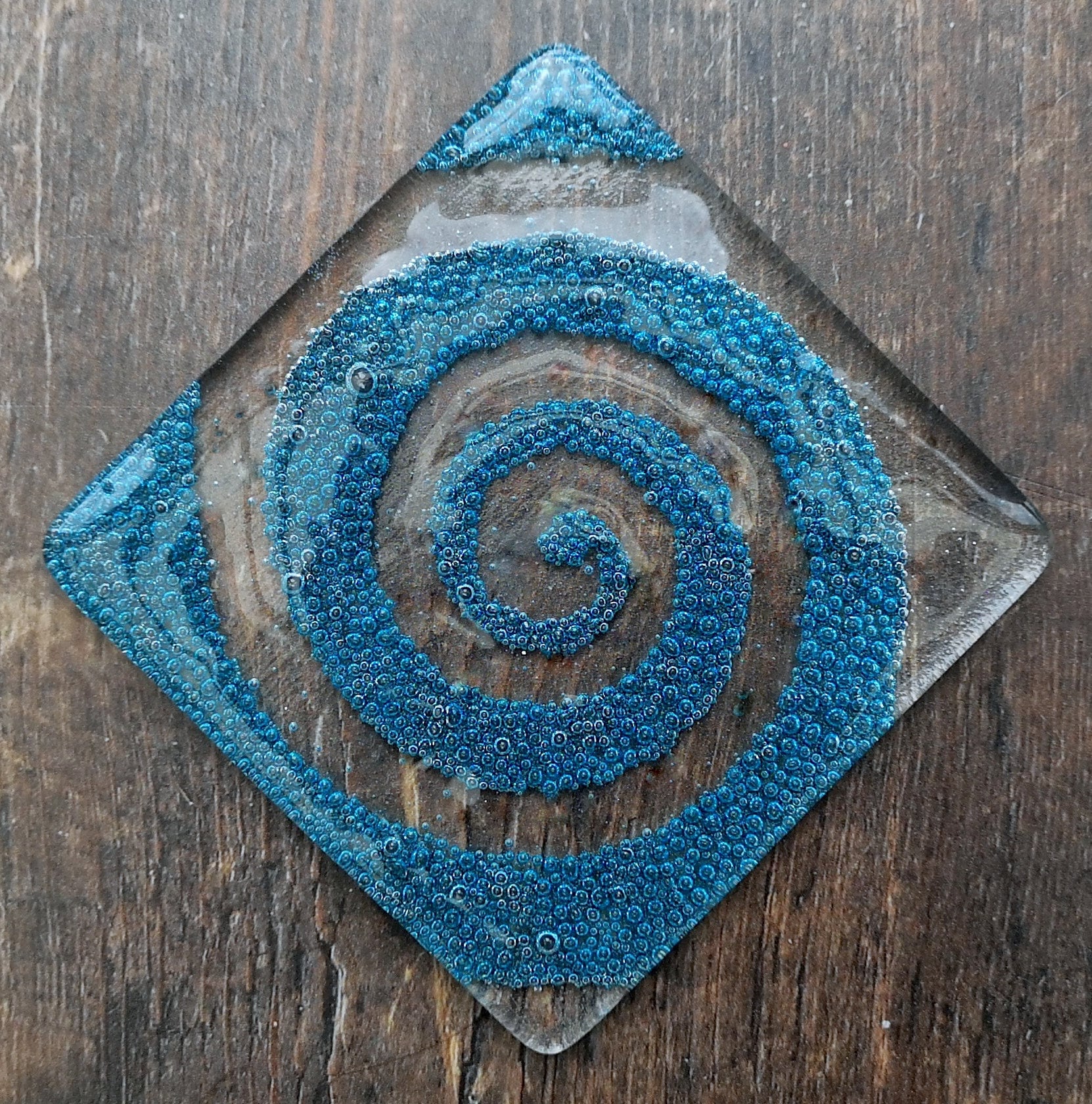 Handmade fused glass spiral drinks coaster with embedded coloured bubbles. Glass wall tile, hot drink table mat, twirl design, swirly pattern gift. Bubbly home decoration, dining table protection.