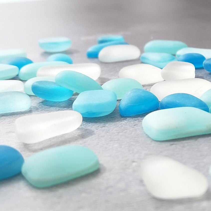 Close-up of light blue, turquoise, and clear tumbled glass, emphasizing their unique frosted textures and subtle colour differences, ideal for DIY projects
