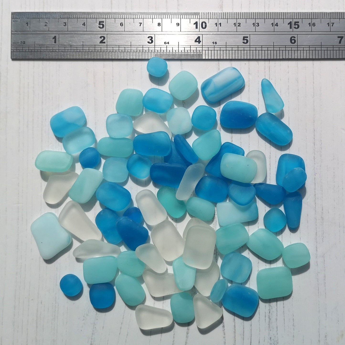 Vibrant and calming tumbled glass assortment in blues and clear tones on a white surface, focusing on the raw, frosted texture perfect for art projects