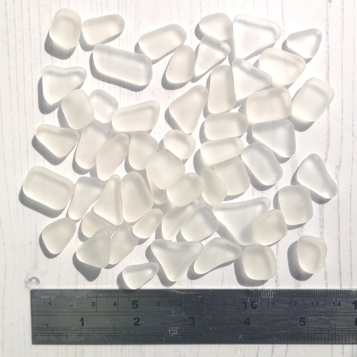 Clear tumbled glass in various sizes, showcasing their frosty, sea glass-like finish and decorative potential. Arranged to spark crafting ideas, emphasizing their size variety and elegant simplicity.