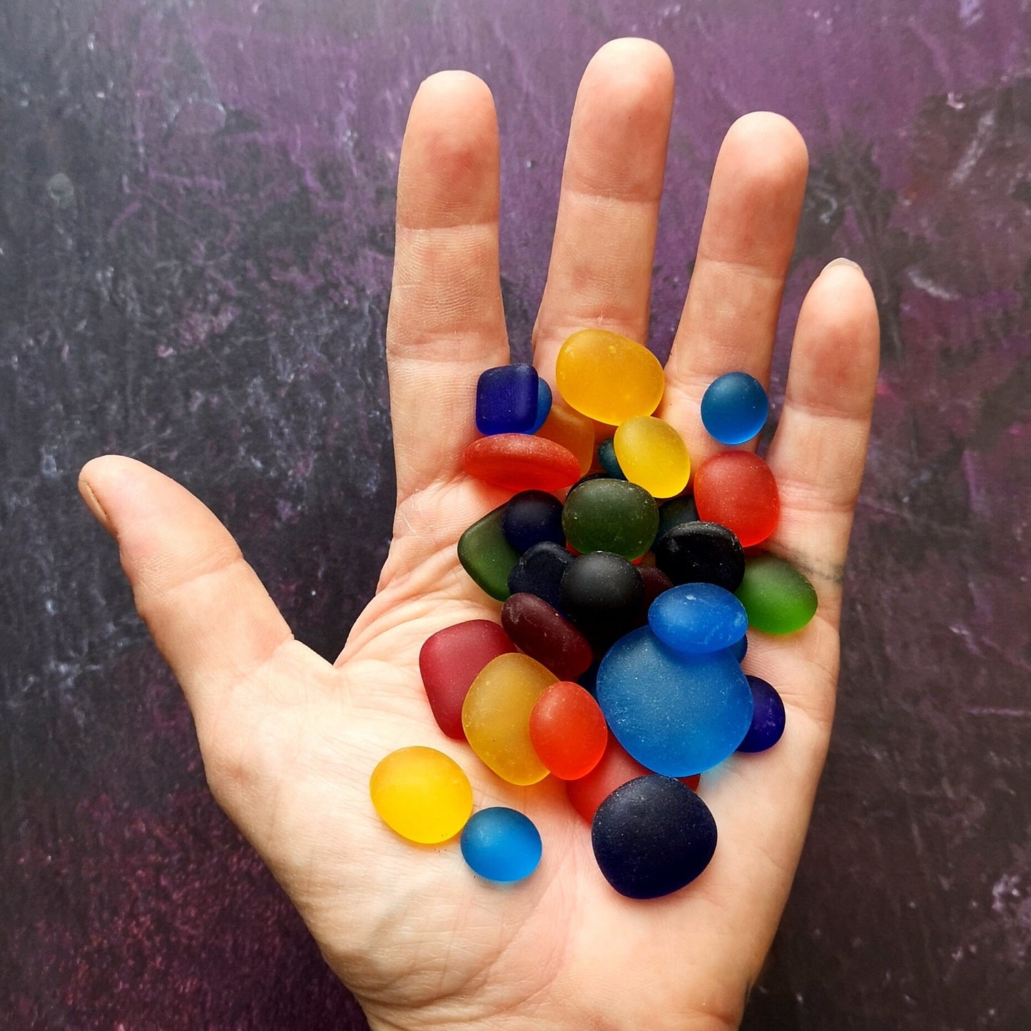 A handful of rainbow-coloured tumbled glass pieces, with an emphasis on their unique, weathered appearance, ideal for custom artwork