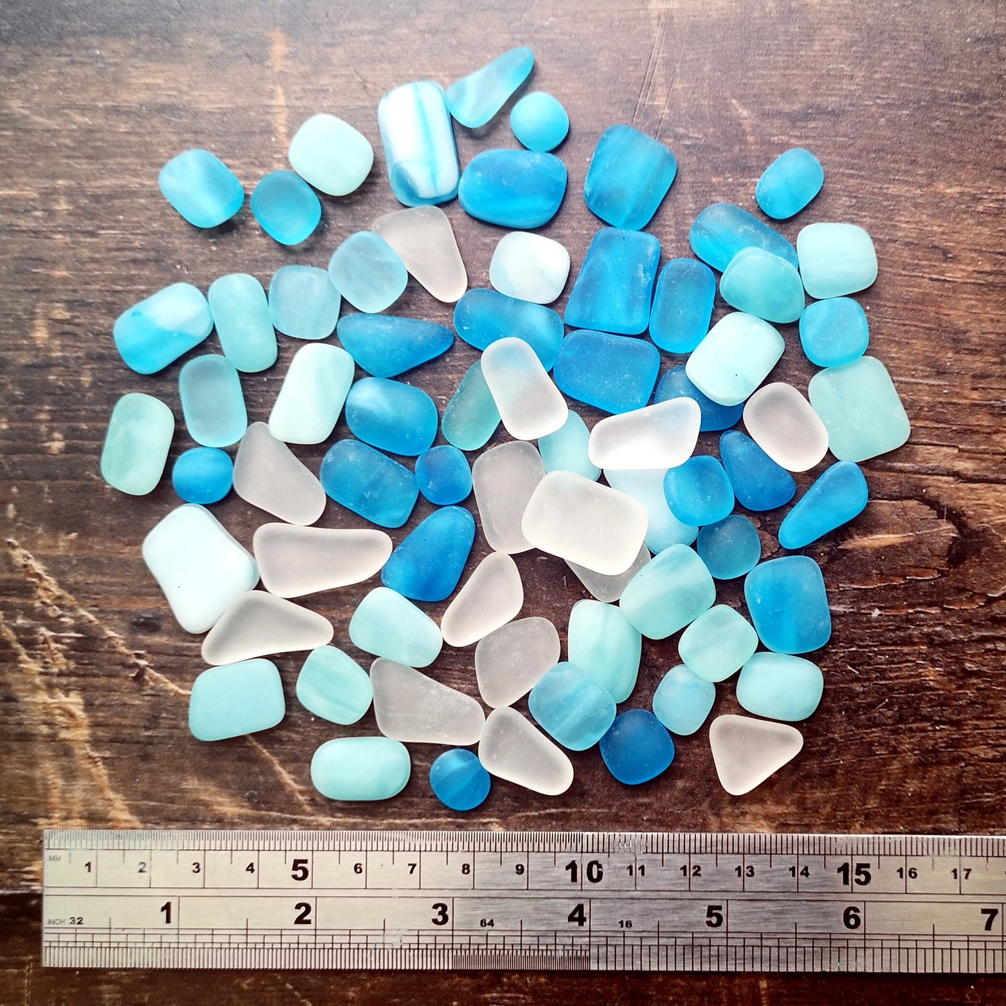 Tranquil hues of light blue and turquoise tumbled glass, complemented by clear pieces, laid out on a dark surface, showcasing their frosty sea glass finish