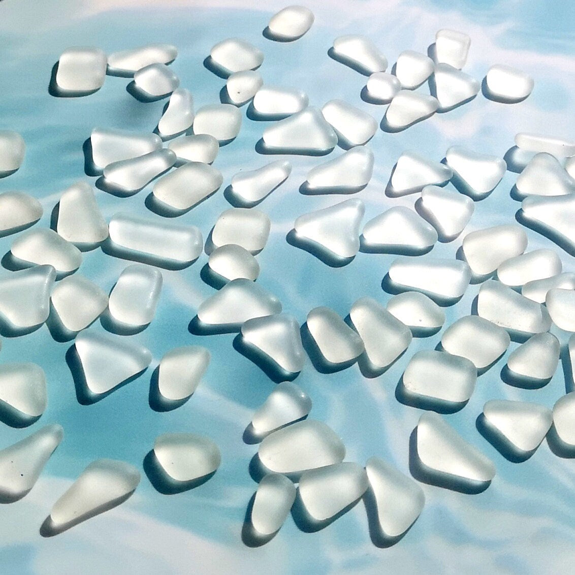 Clear tumbled glass assortment with a frosty white finish, spread on a bright surface, focusing on their raw texture ideal for artistic designs