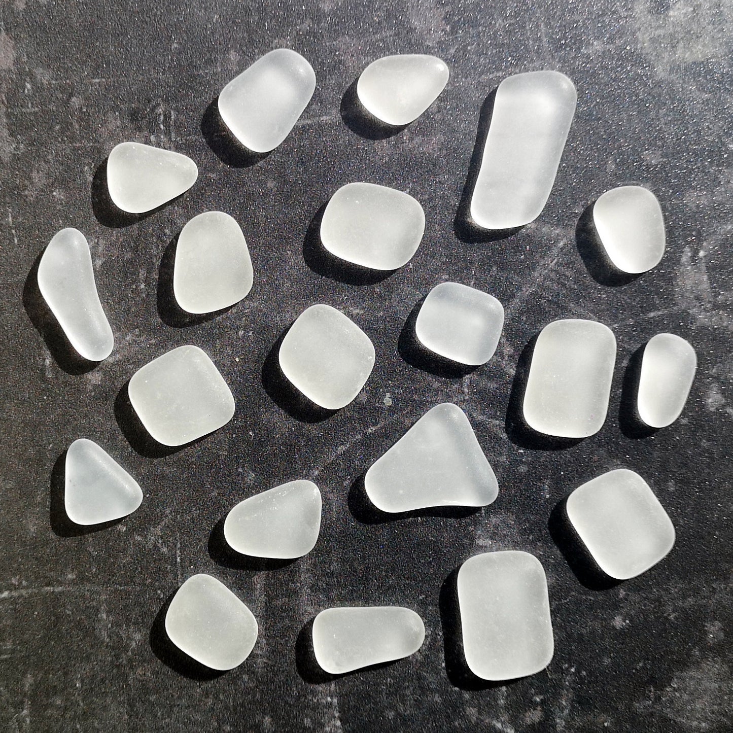 Elegant array of clear tumbled glass in different sizes, arranged neatly, emphasizing their frosted surface and potential for creative DIY projects