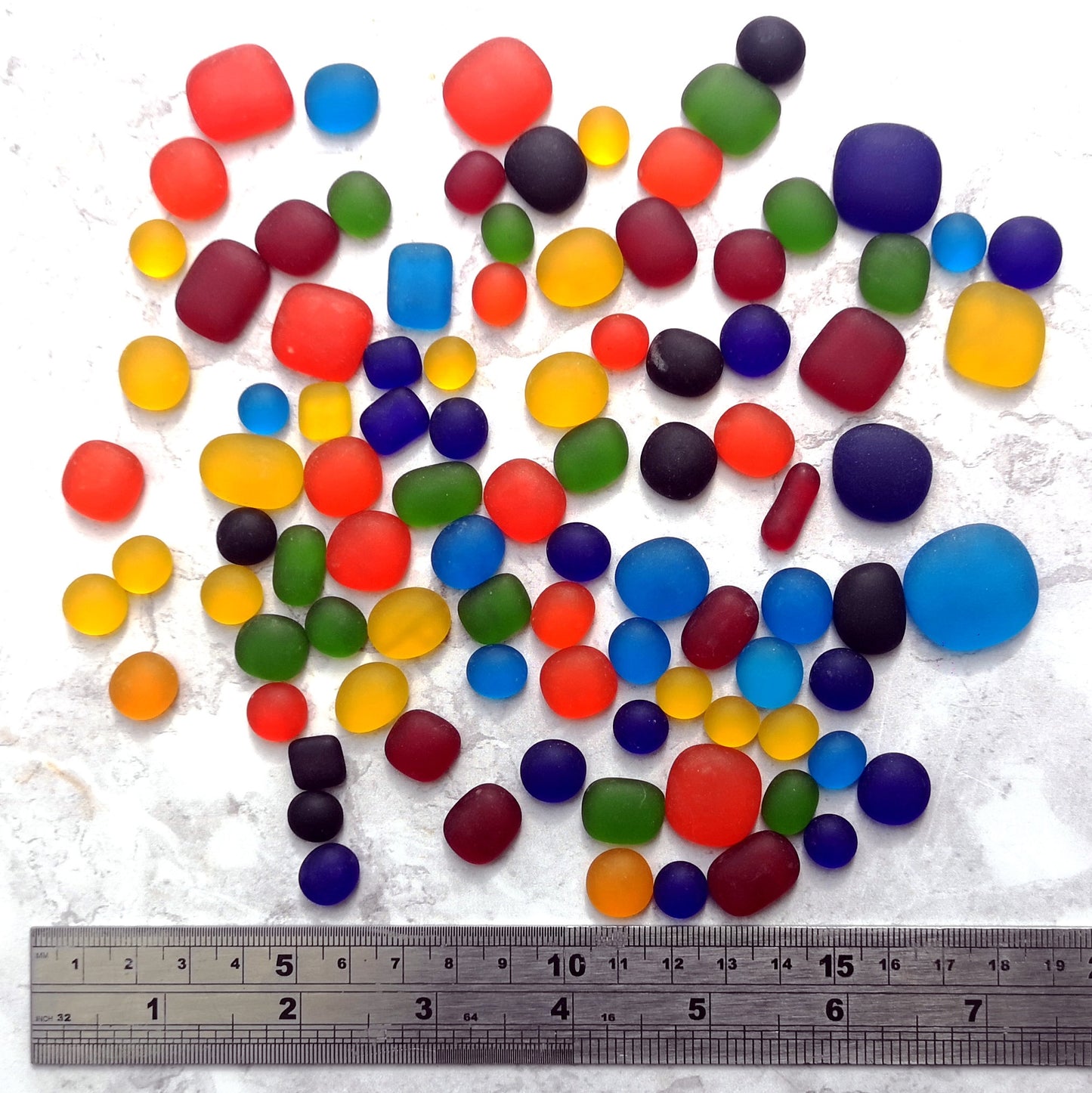 A collection of weathered sea glass-like tumbled pieces in rainbow colours, scattered on a light surface, ideal for crafting and decoration. Gift for