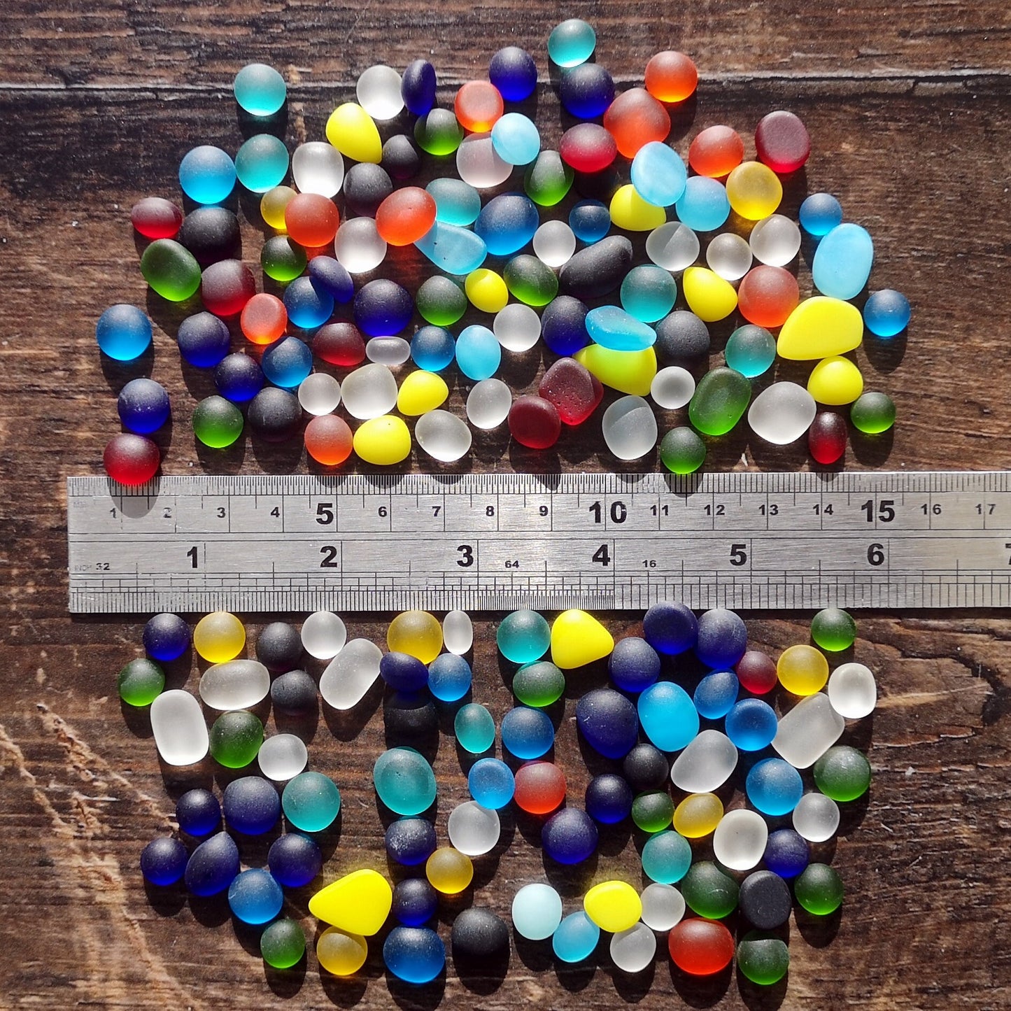 Assorted tiny tumbled glass in a rainbow of colors, neatly arranged in a gradient, emphasizing their diverse sizes and potential for creative use
