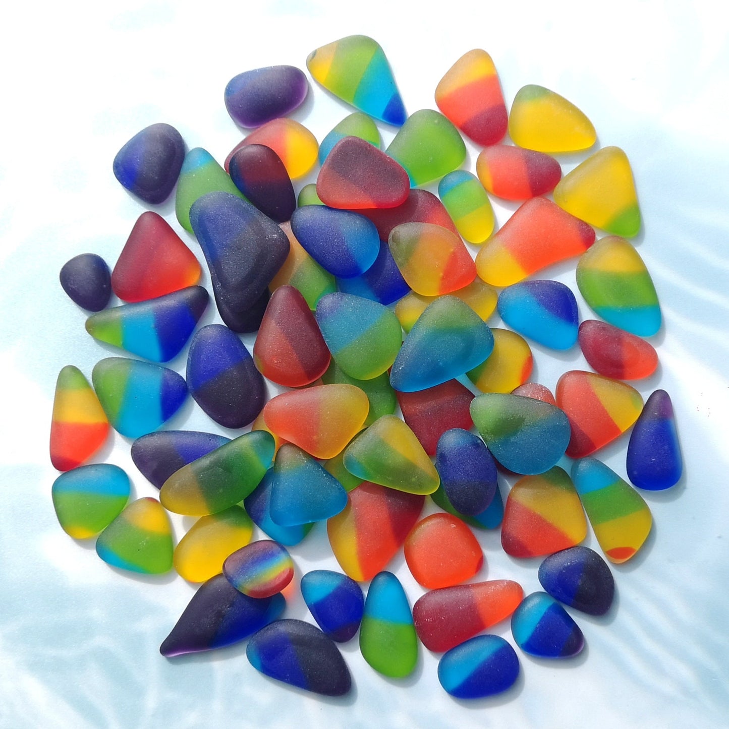 Pile of weathered, frosted sea glass-like tumbled pieces in a multitude of colors, set against a neutral background for a striking contrast