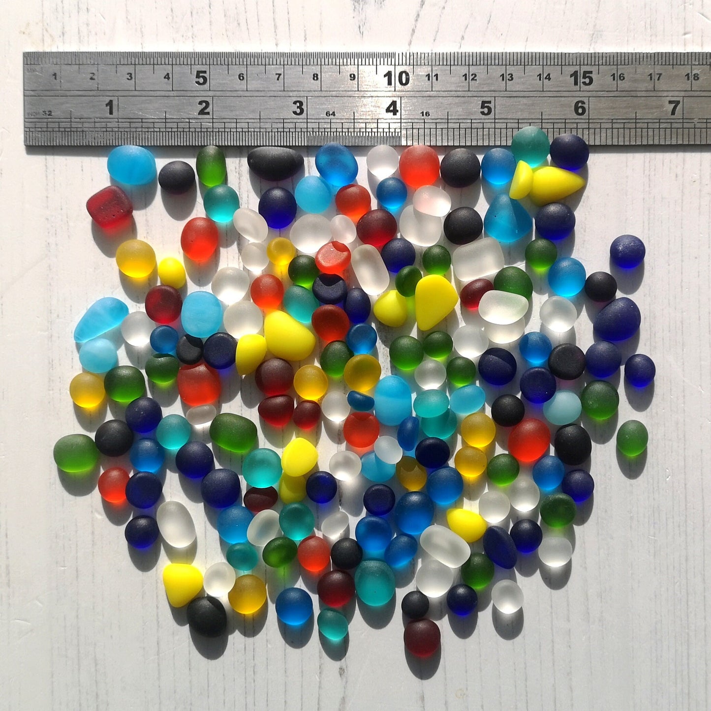 Vibrant and colorful tiny tumbled glass pieces scattered on a white background, emphasizing their raw, unpolished beauty for creative projects