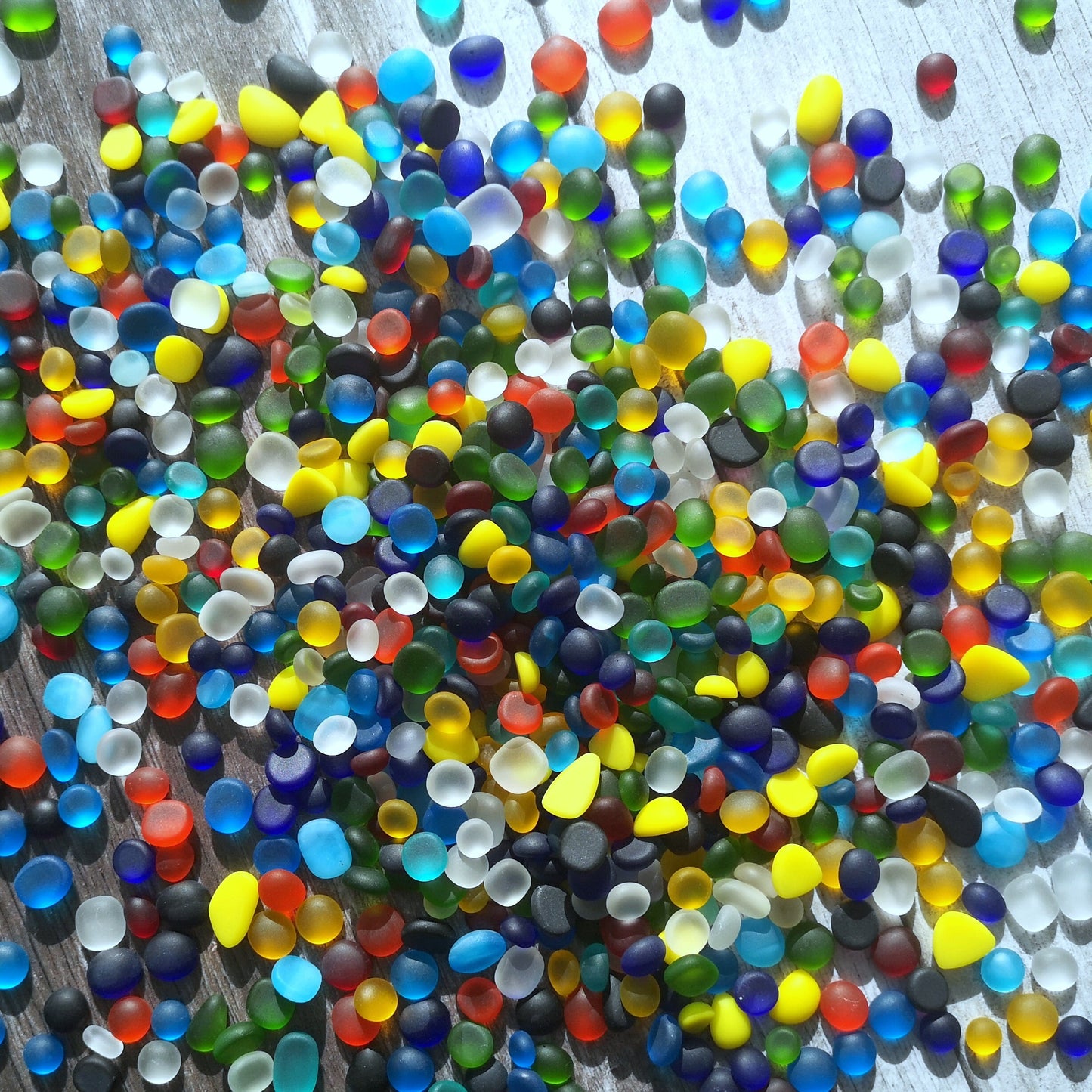 Artistic display of tiny, multicoloured tumbled glass, set out to inspire creative DIY projects, emphasizing their size variety and visual appeal