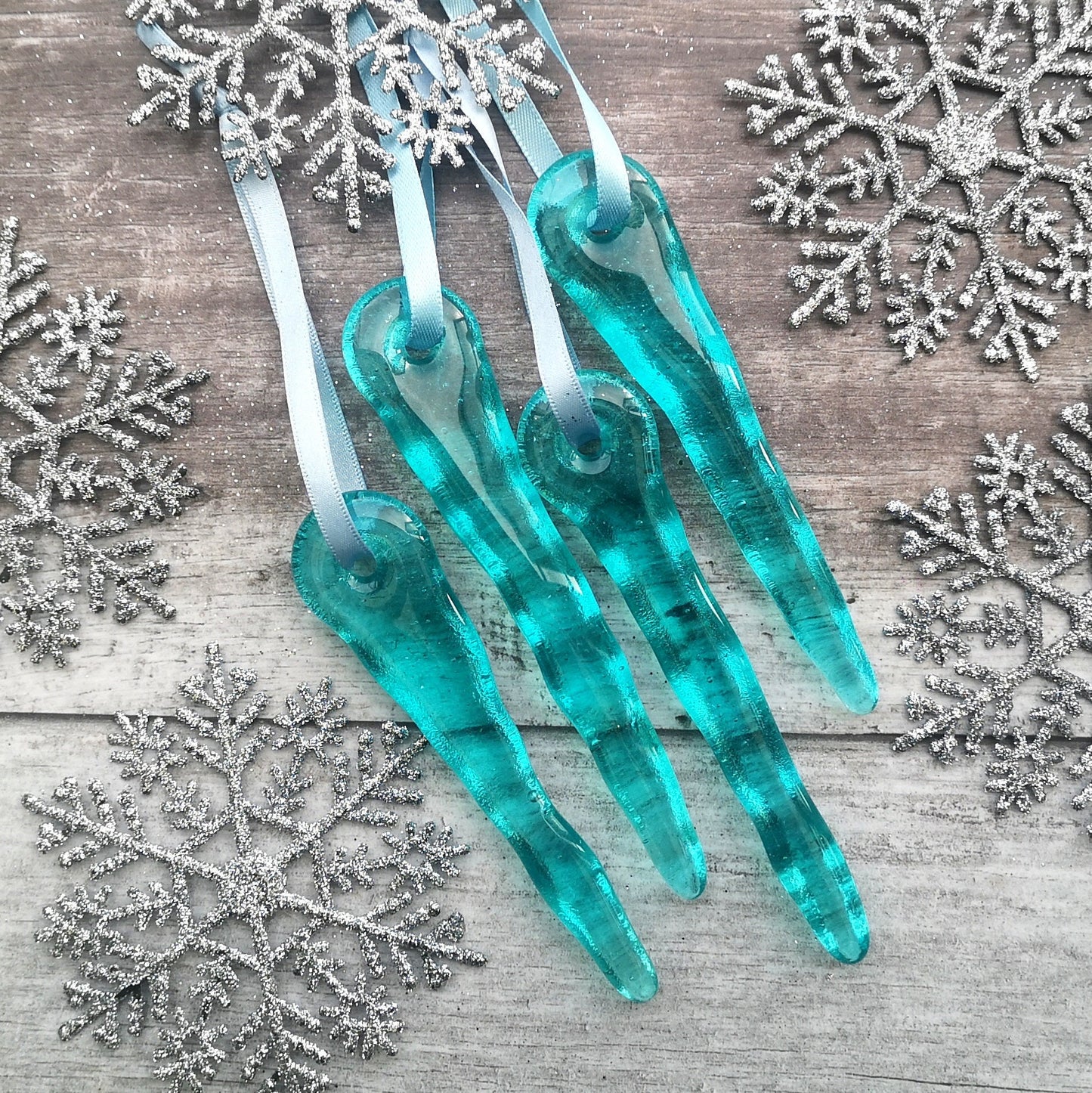 Handmade aqua blue glass icicle ornaments, surrounded by festive snowflakes, showcasing their unique charm and craftsmanship