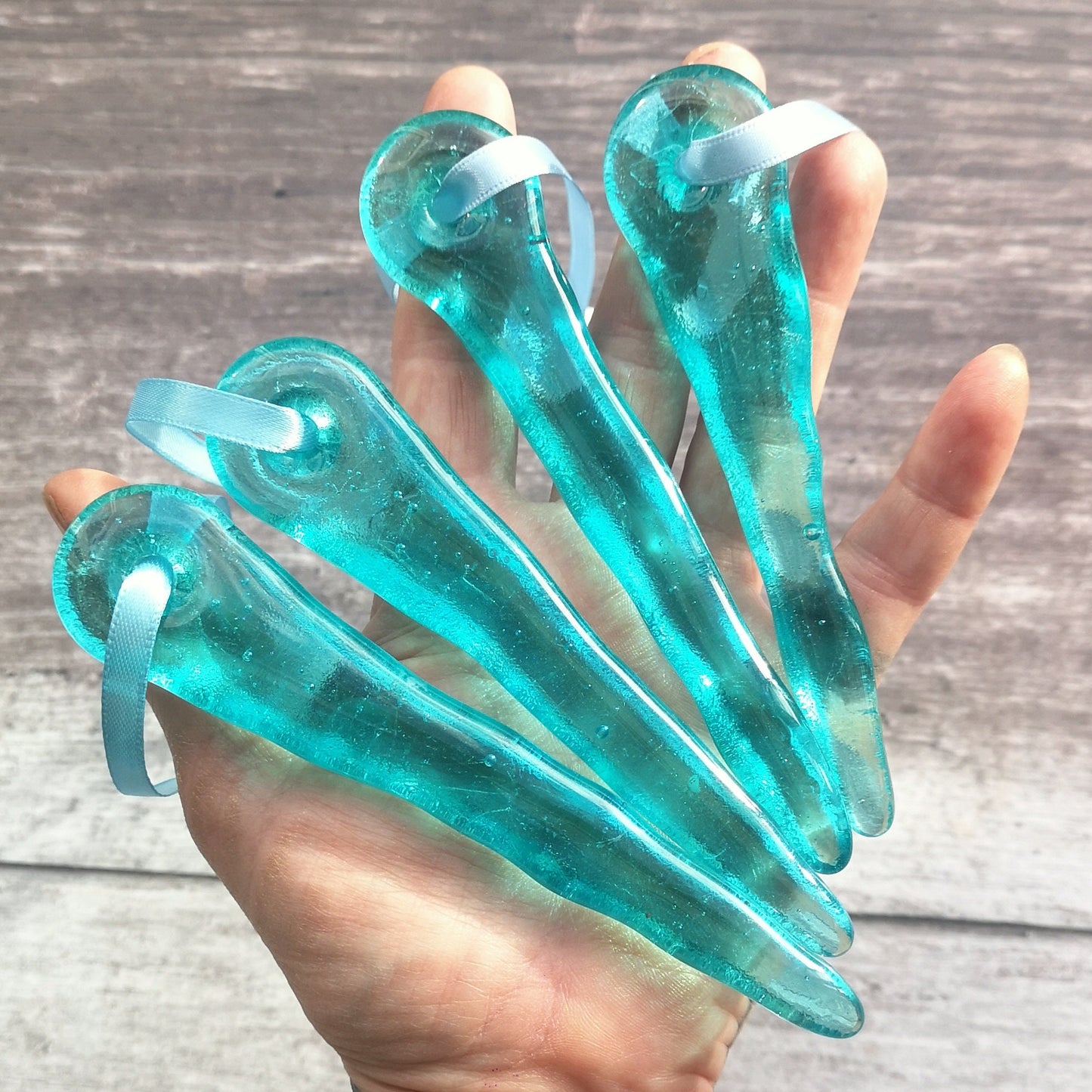 A hand full of aqua blue glass icicle ornaments, captured in close-up to show their size and highlight their shape and transparent beauty