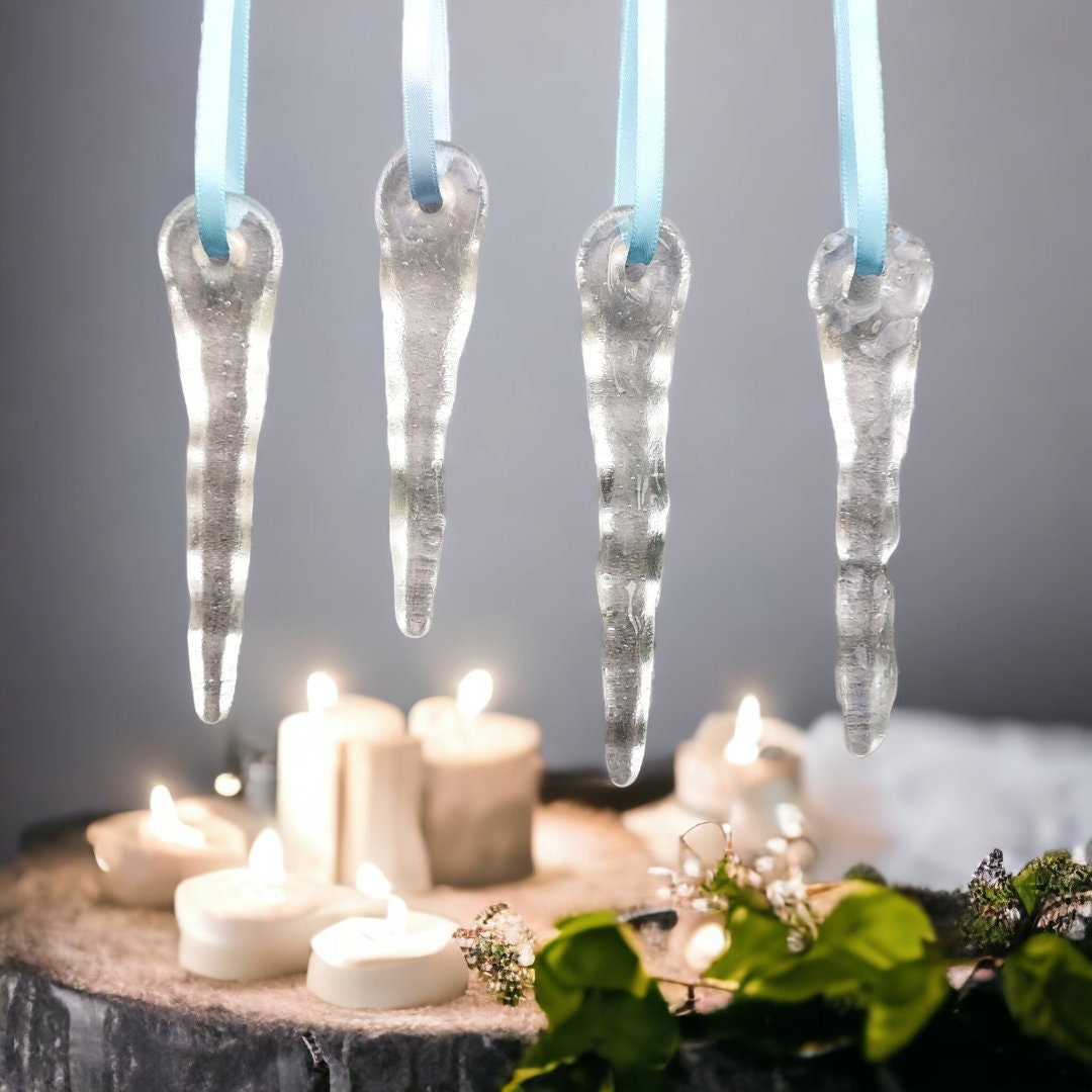 Four handcrafted glass icicle decorations hanging against a festive candle background, showcasing the clear option