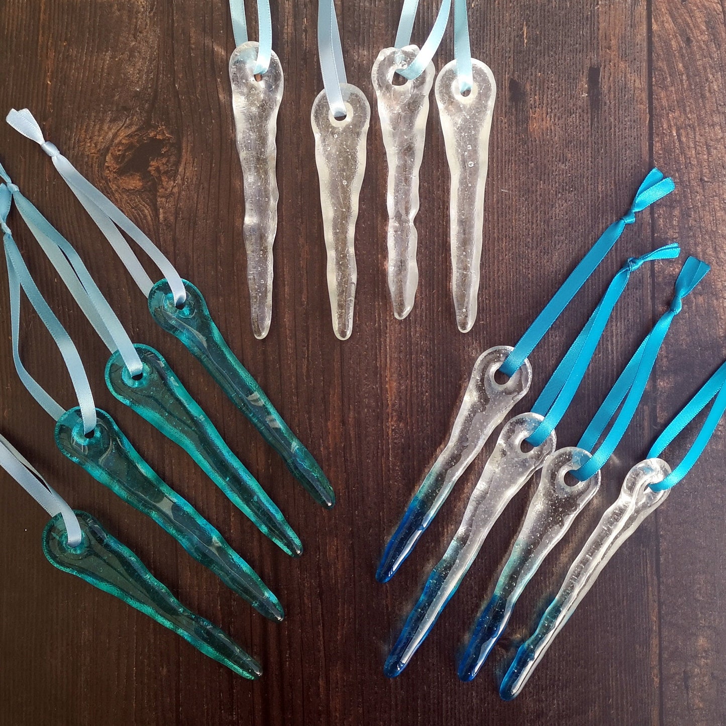 Assortment of glass icicles in clear, aqua blue, and with blue tips, neatly lined up, demonstrating the variety and quality of the handmade pieces