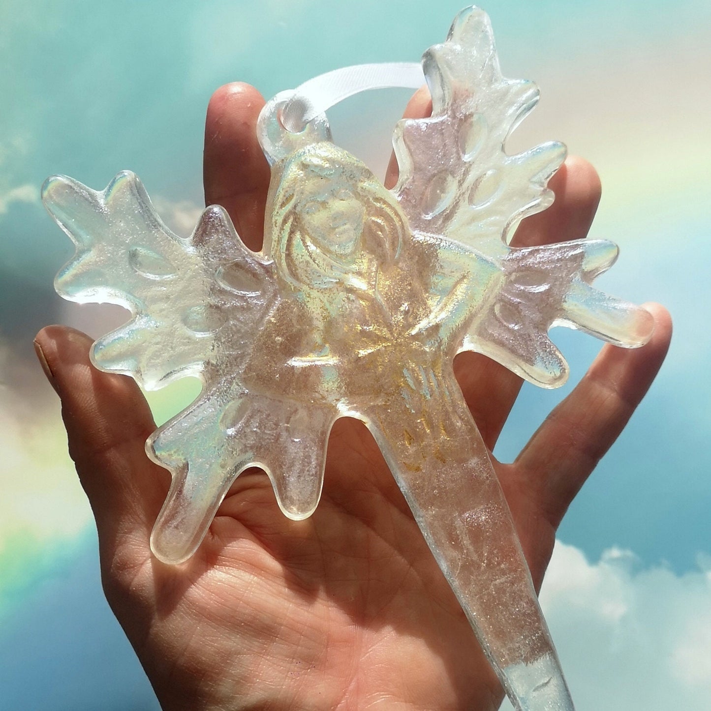 An angel wings / fairy icicle hanging decoration, against a hand to show size, with natural light enhancing its translucent and icy appearance