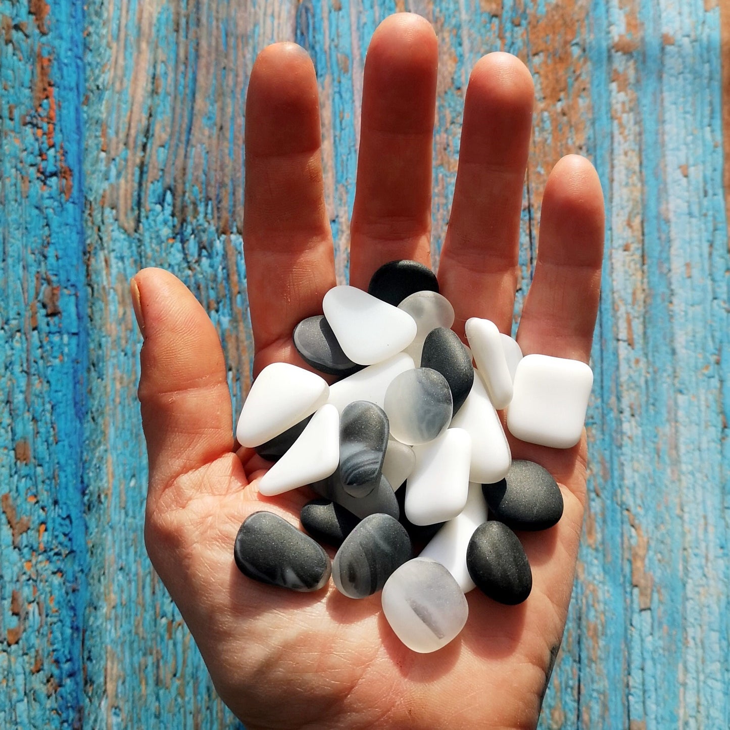 A handful of White and Black frosted tumbled glass pieces with some clear tones, capturing their subtle beauty and suitability for unique art creations.