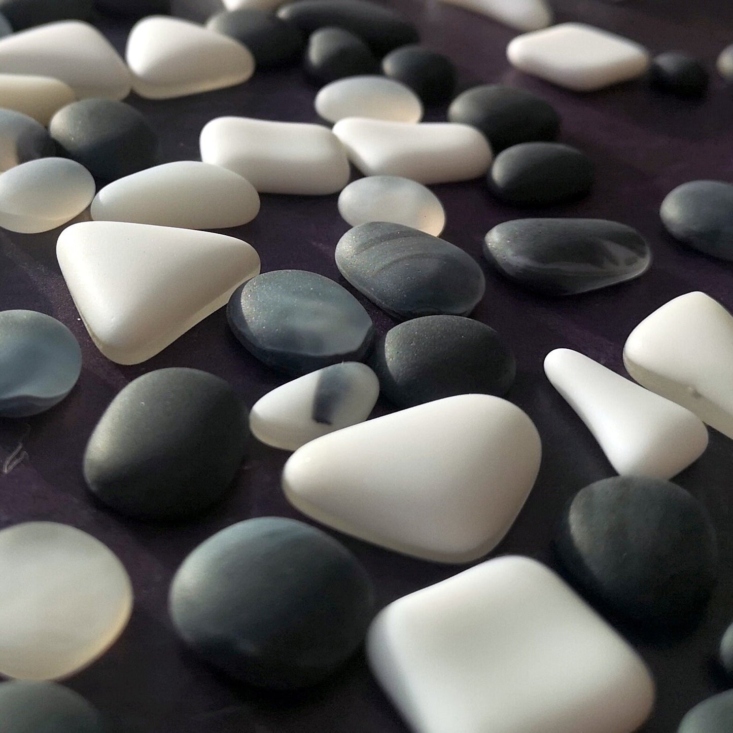 Close-up of various-sized black and white tumbled glass pieces, highlighting their unique frosted textures and resemblance to naturally weathered sea glass.