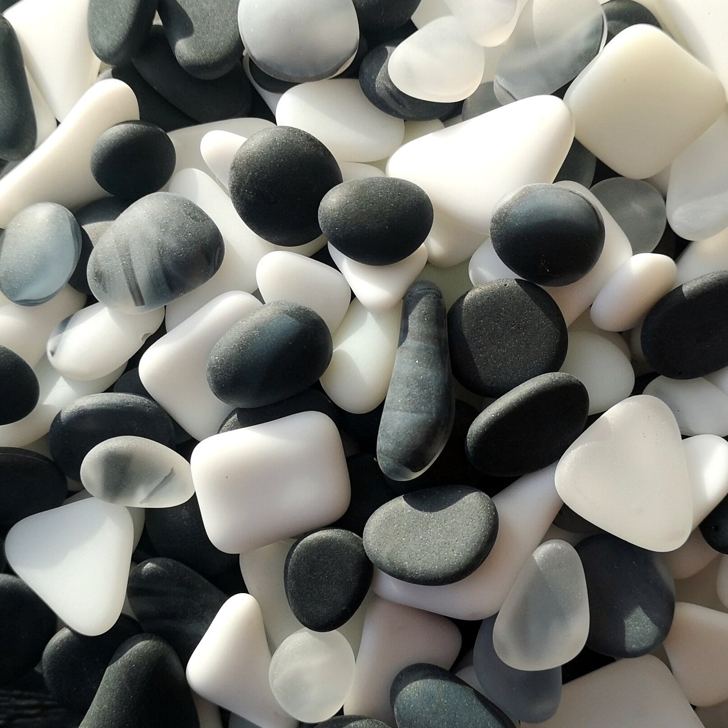 Pile of frosted white and black tumbled glass pieces, resembling weathered sea glass.