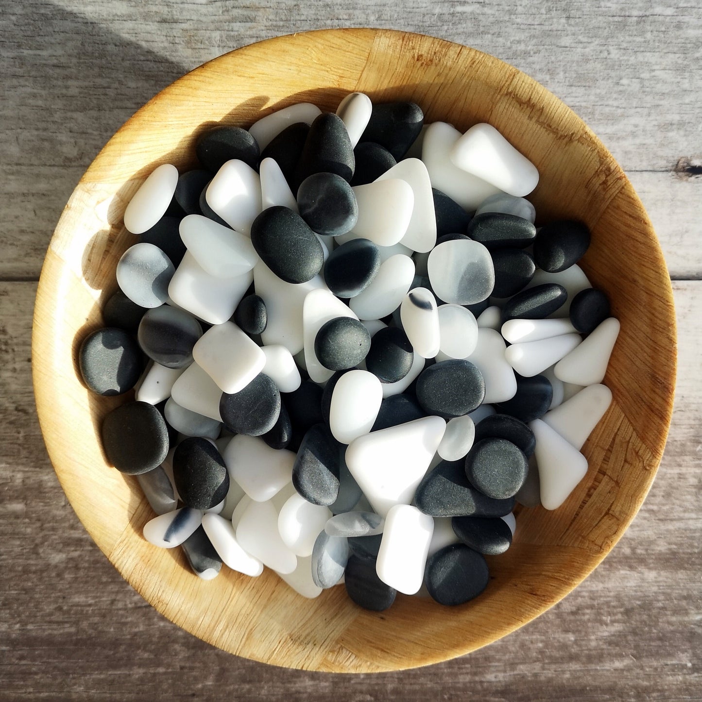 Black and white frosted tumbled glass, carefully arranged in a bowl to spark crafting ideas, emphasizing their size variety and elegant simplicity