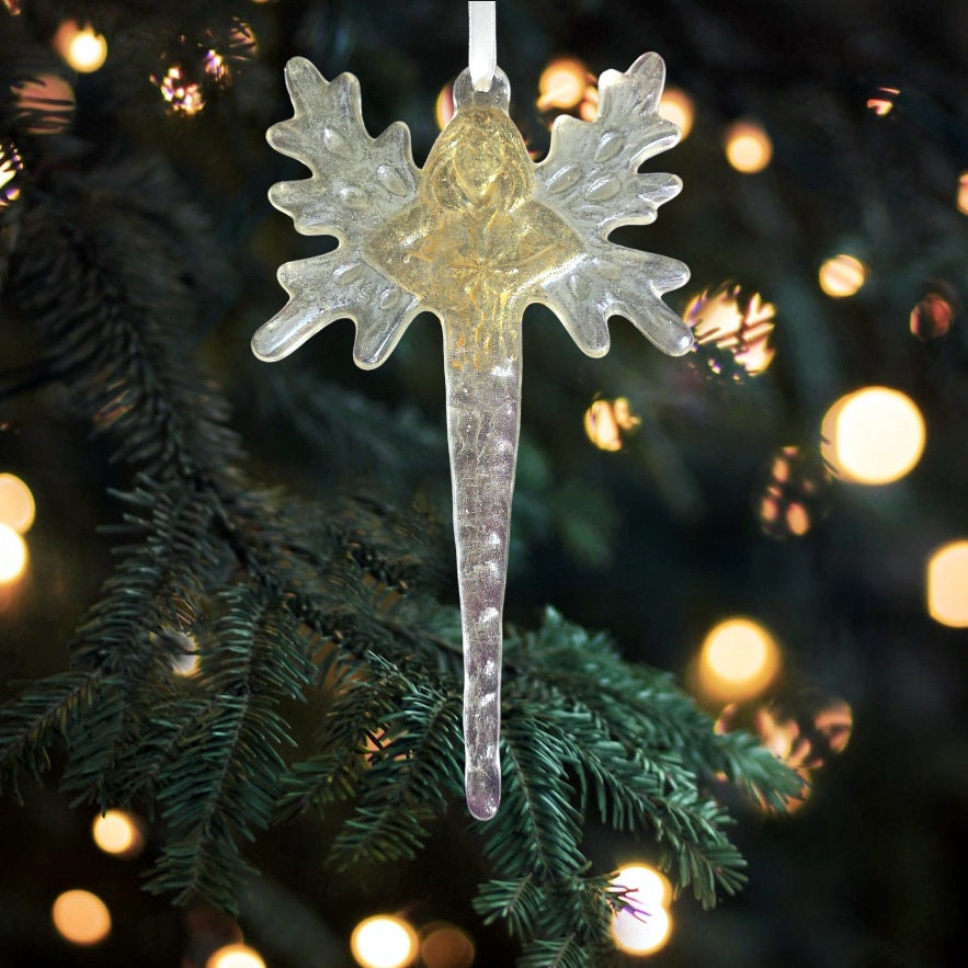 Glass angel wings or fairy icicle against a soft, blurred Christmas tree background, emphasizing its ethereal beauty.