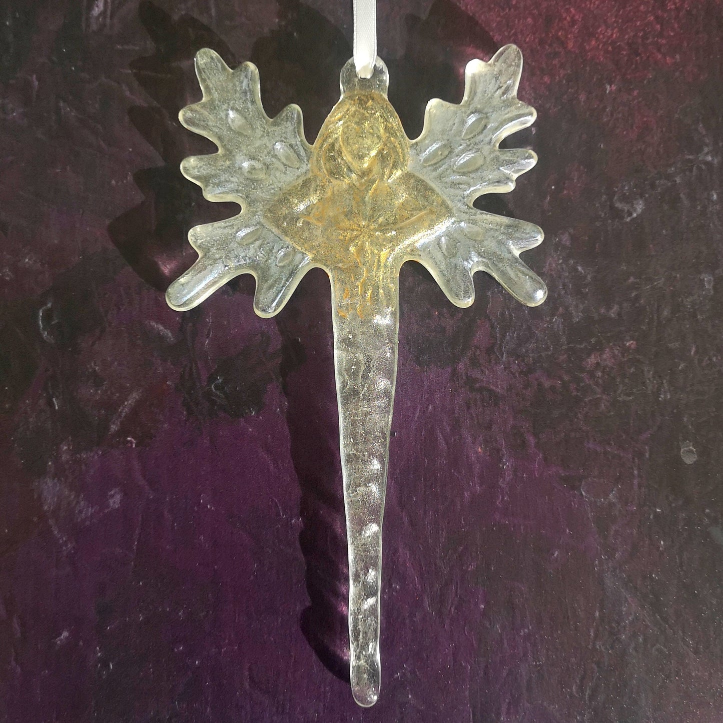 Glass fairy or angel icicle ornament displayed against a dark background, focusing on its highlighted gold colour.