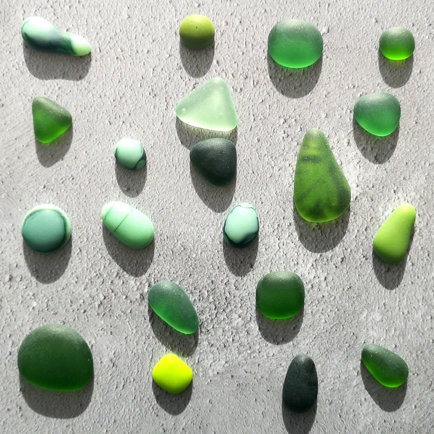 Green-coloured tumbled glass assortment, neatly arranged, emphasizing their diverse sizes and potential for artistic use