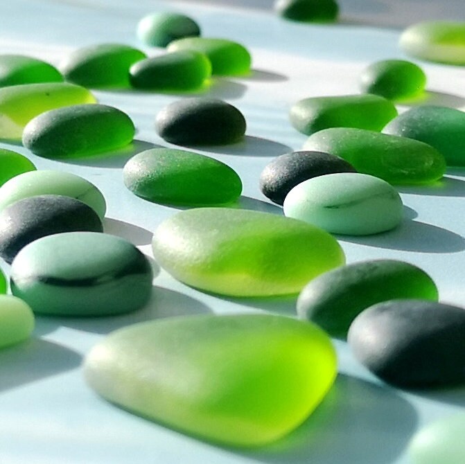 Close up display of green coloured tumbled glass, arranged to inspire artistic endeavours, emphasizing their size variety and colourful charm