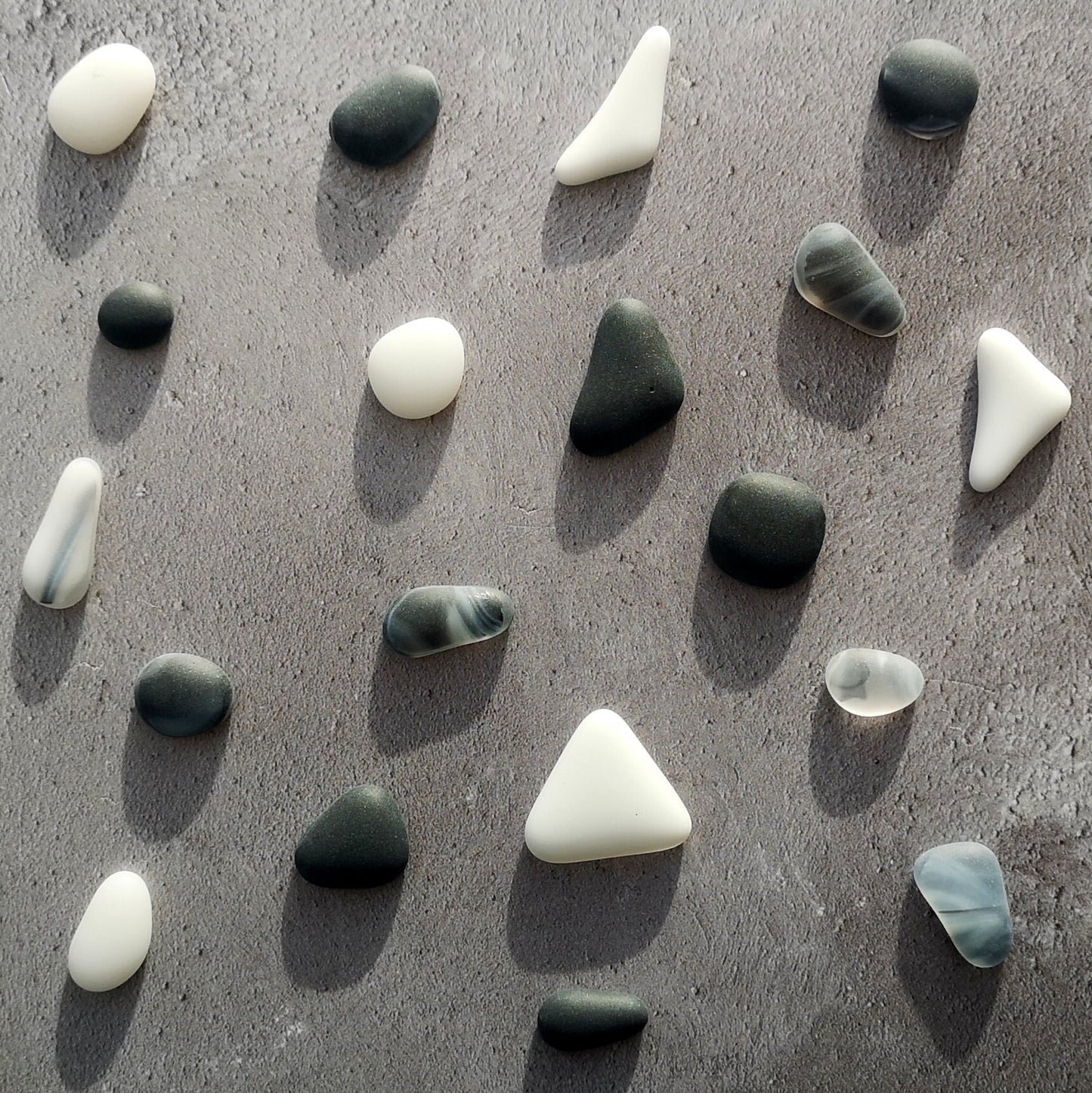 Array of black and white tumbled glass in different sizes and shapes, arranged neatly, emphasizing their frosted surface and potential for creative DIY projects.