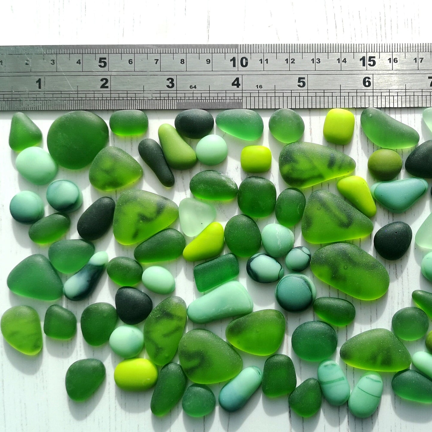 A collection of weathered sea glass-like tumbled pieces in green colours, scattered on a light surface, ideal for crafting and decoration