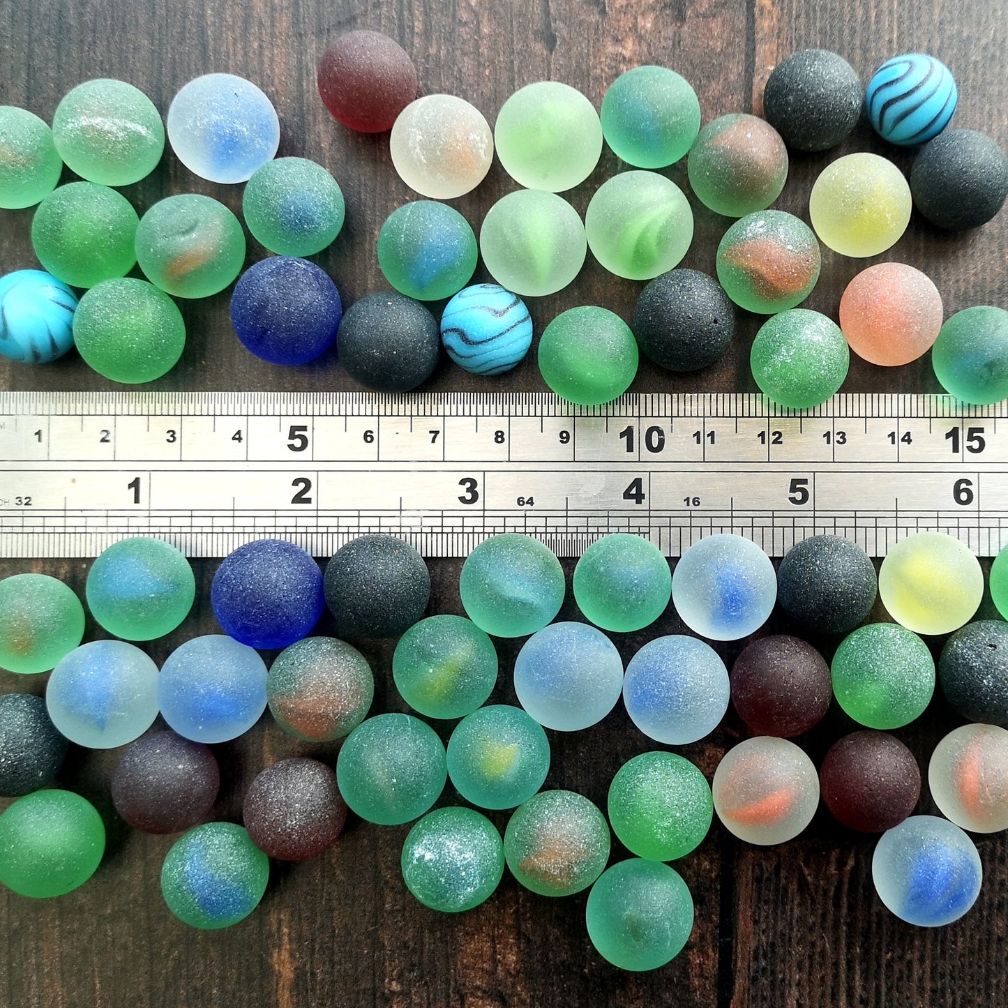 Vibrant and colourful tumbled glass marble pieces scattered on a dark wood background, emphasizing their size and raw, unpolished beauty for creative projects