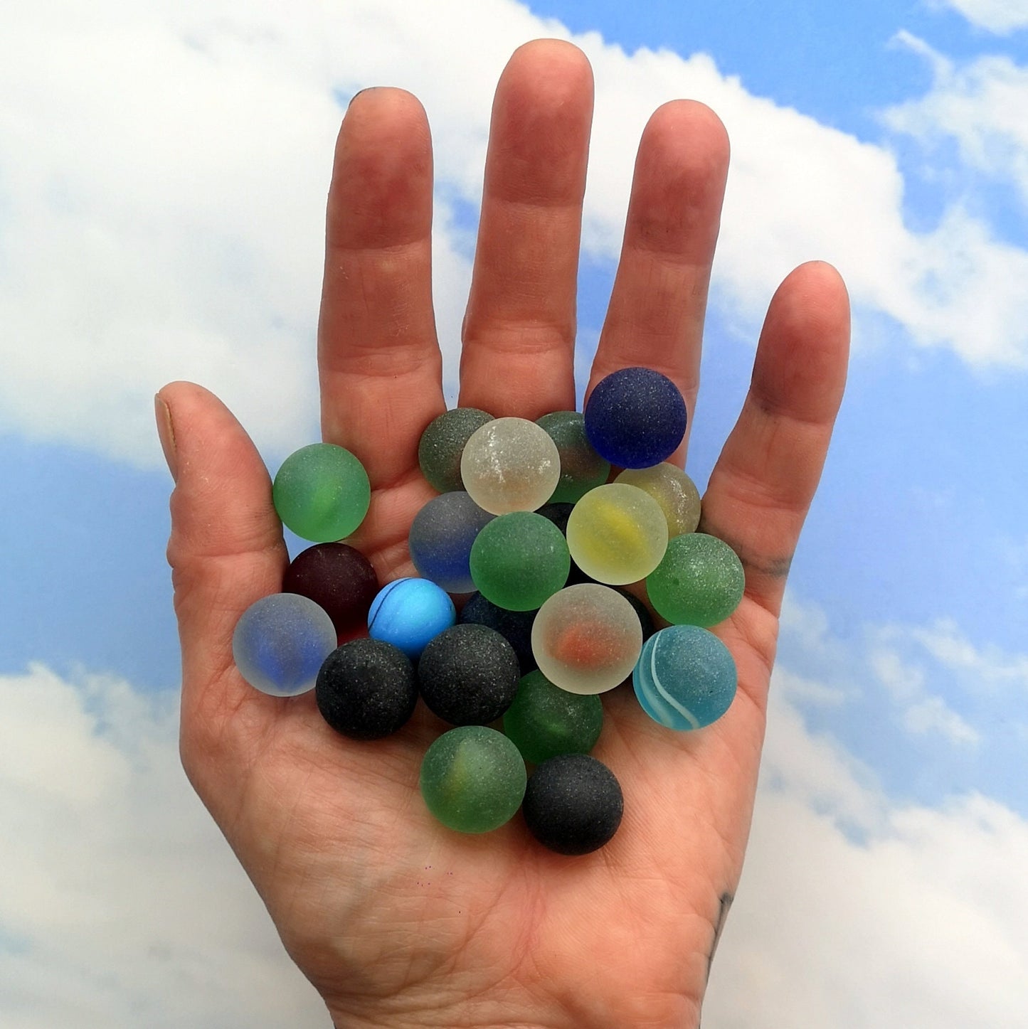 A handful of mixed tumbled glass marble pieces, with a focus on their frosted texture and sea glass look, perfect for custom decoration