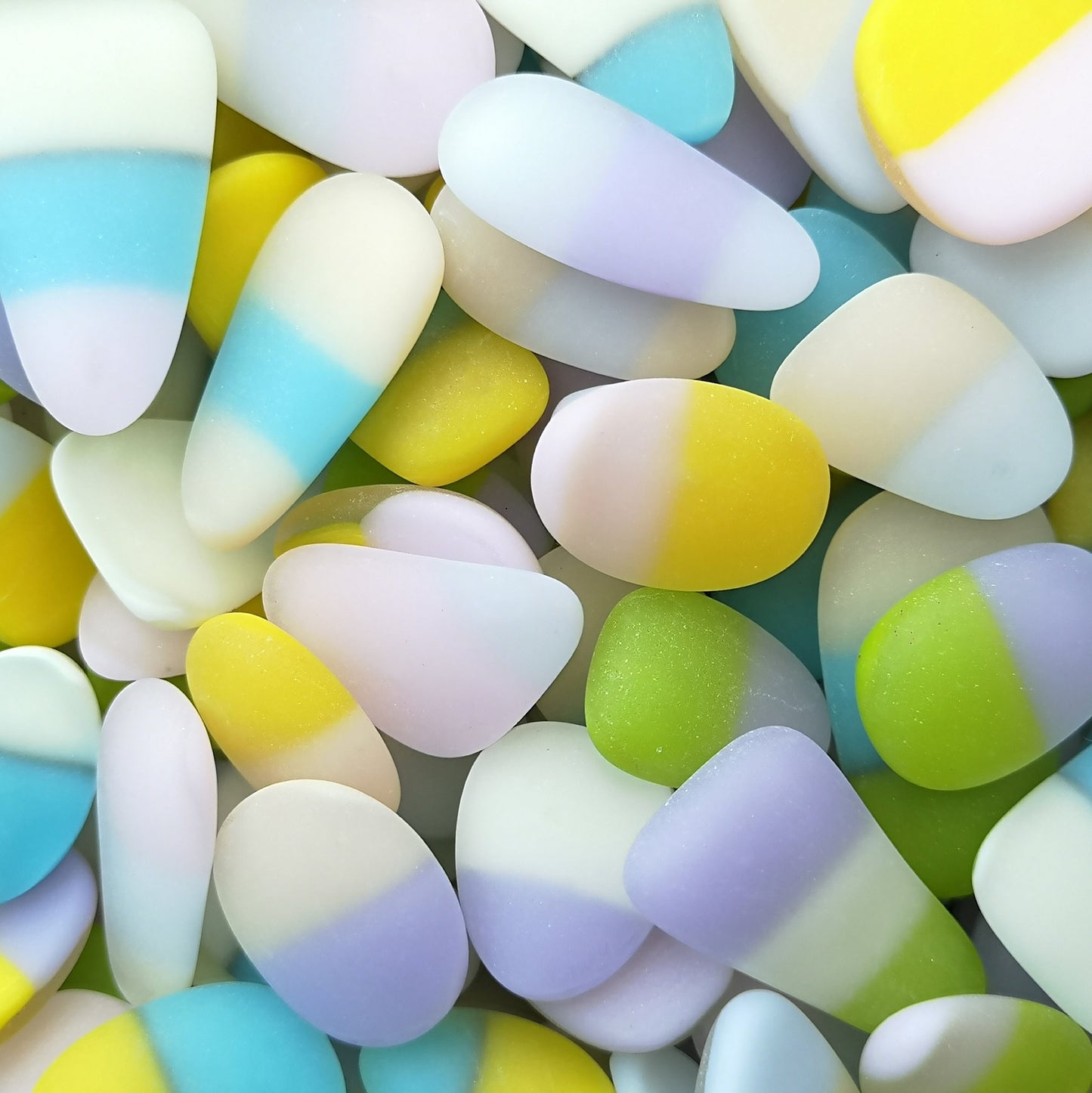 Pile of weathered, frosted sea glass-like tumbled pieces in a multitude of colours, set against a neutral background for a striking contrast