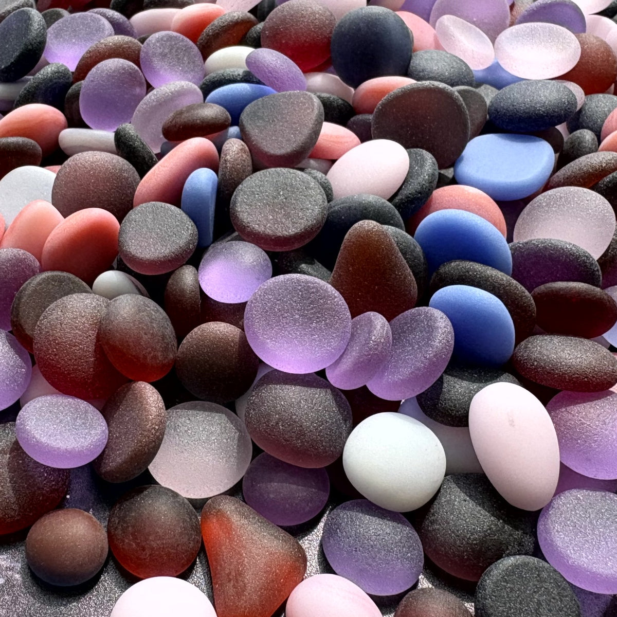 A dense pile of smooth, polished pebbles and sea glass stones in many colors including purple, pink & blue.