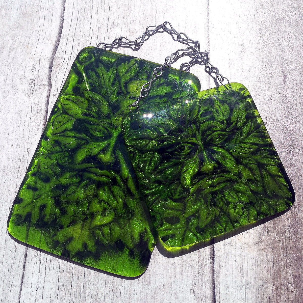Two green glass hanging ornaments with a Leaf Man design, hung on silver chain, displayed on a light grey wood background. Nature or Pagan gift. 